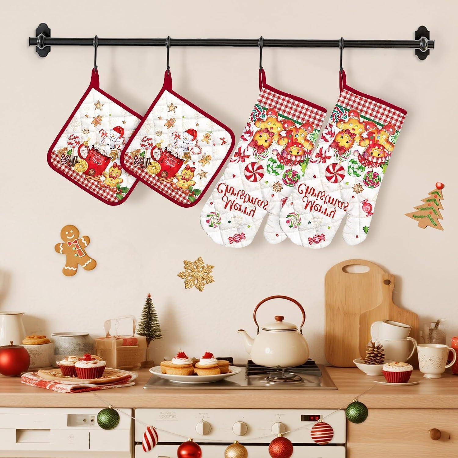 Weihnachtliche Küchenausstattung mit zwei roten Topflappen und zwei Weihnachtsofenhandschuhen, die über einer Arbeitsfläche mit Backwaren, Teekanne, Geschirr und festlicher Dekoration hängen.