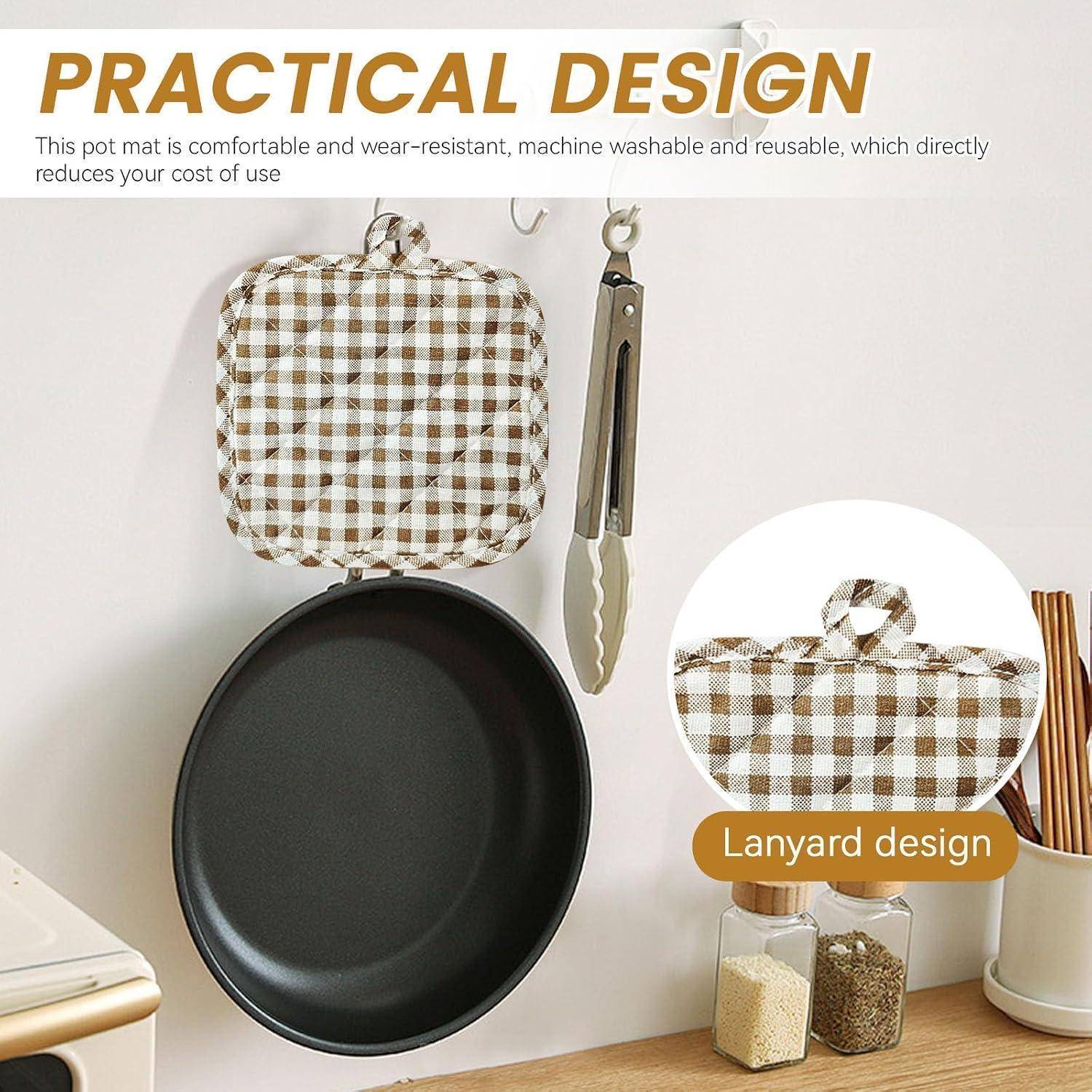Werbebild einer Gingham-Topfunterlage mit Trageschleife, dargestellt hängend neben Küchenzangen und einer schwarzen Pfanne; der Text sagt „PRAKTISCHES DESIGN