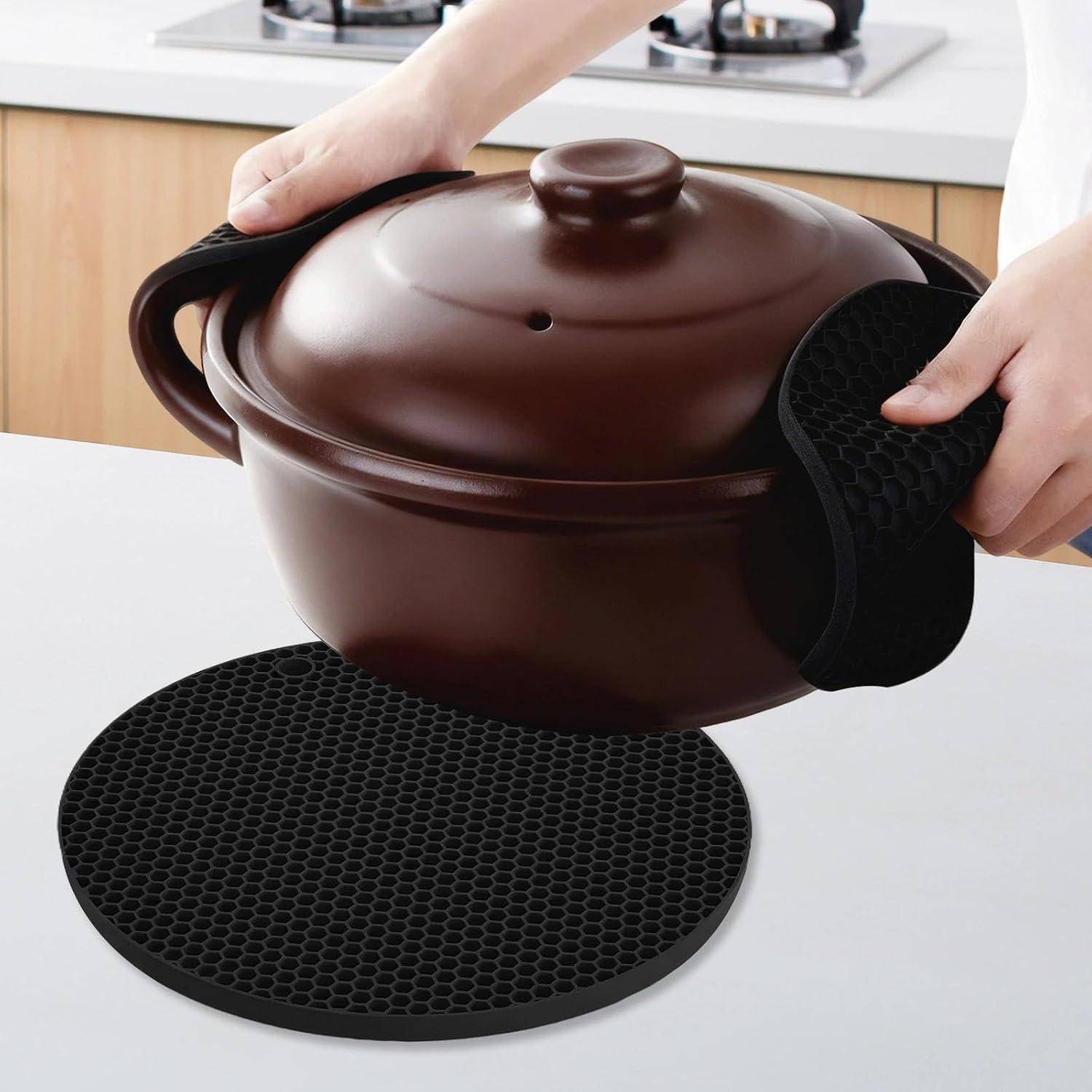 Hände heben einen braun abgedeckten Topf an, wobei schwarze Wabenmuster-Topflappen oder Wärmeschutzpolster verwendet werden, um zu greifen und vor Hitze zu schützen.