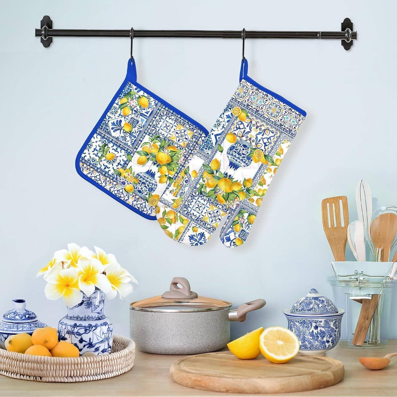 Küchenszene mit blau-weißen zitronenmusterten Ofenhandschuhen und Topflappen, die über einer Arbeitsplatte mit Kochgeschirr, Zitronen, Blumen und Utensilien hängen.