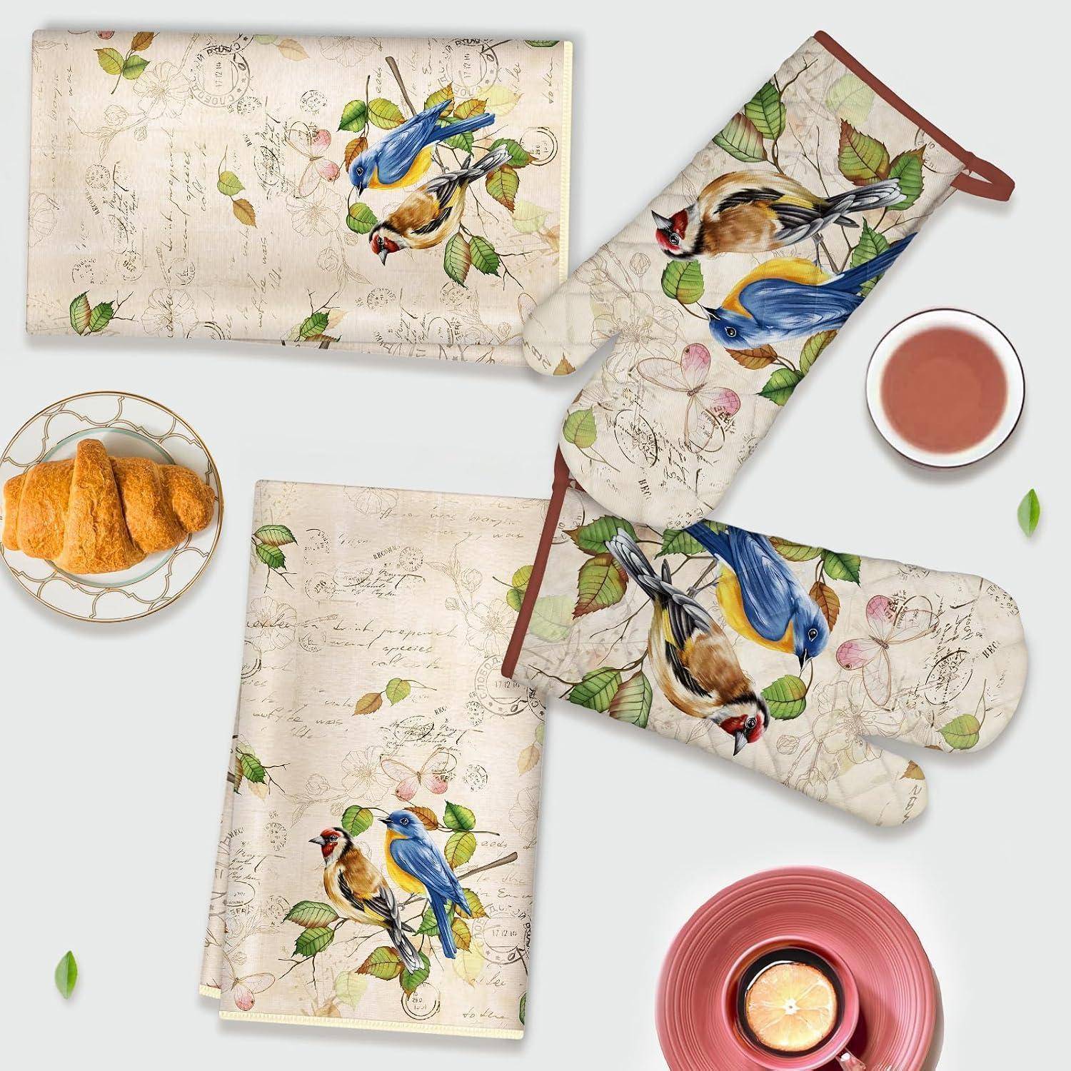 Vogel-thematisches Küchentextil-Set mit Blumenschrift-Druck, bestehend aus Ofenhandschuh, Topflappen und zwei Handtüchern, arrangiert mit einem Croissant-Teller und Kaffeetassen.