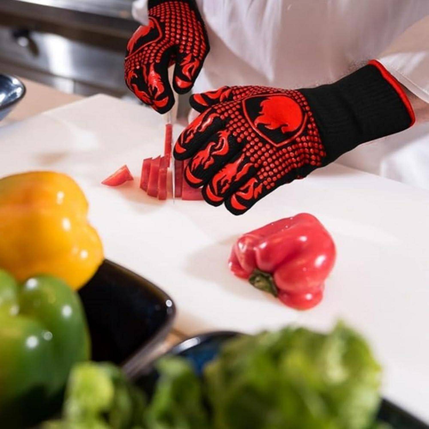 Behandschuhte Hände schneiden eine rote Paprika auf einem Schneidebrett in einer Küche, mit gelben und grünen Paprikas in der Nähe.