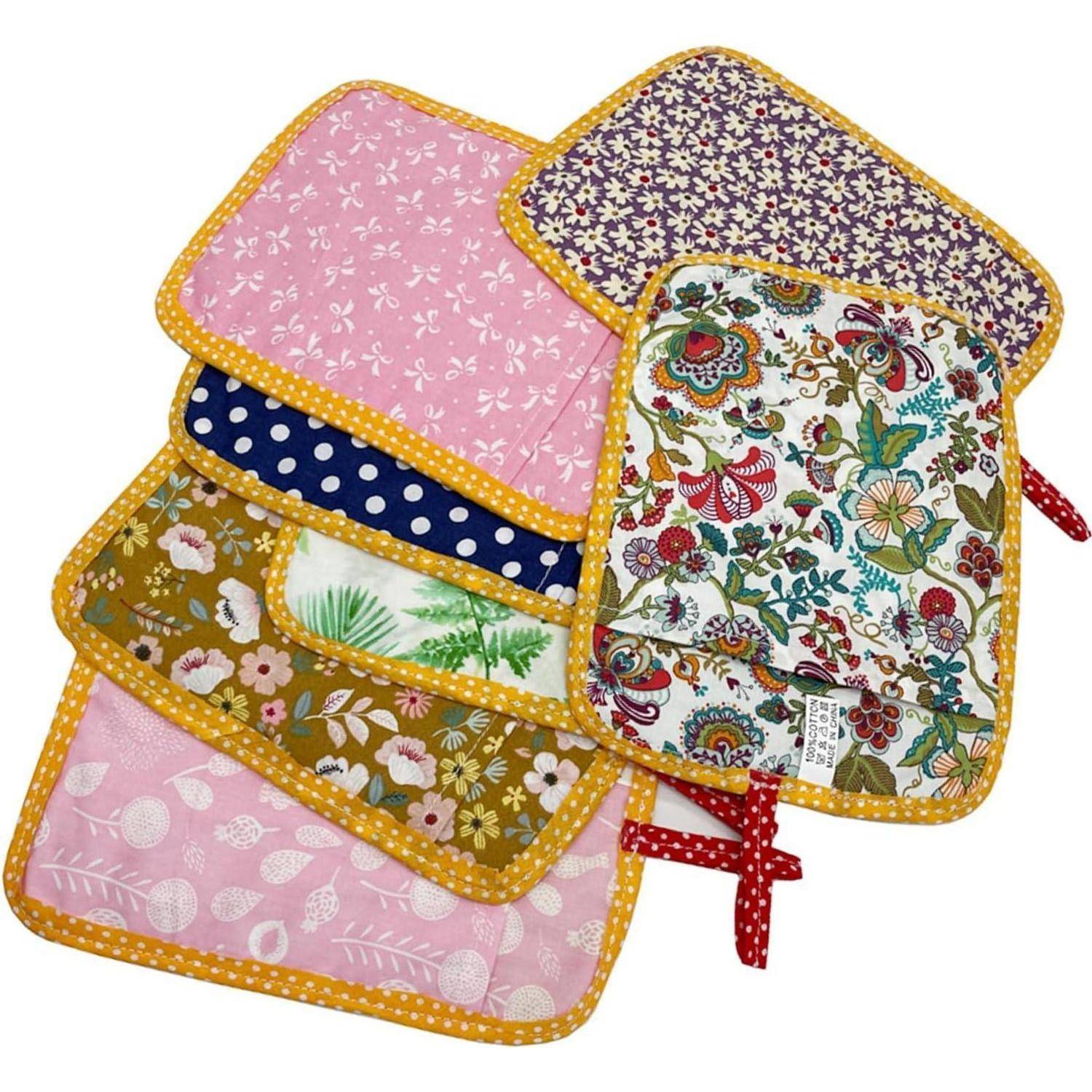 Stapel aus bunten gesteppten Topflappen mit gelbem Besatz, mit verschiedenen Blumen- und Punktmustern, mit roten Bändern gebunden.
