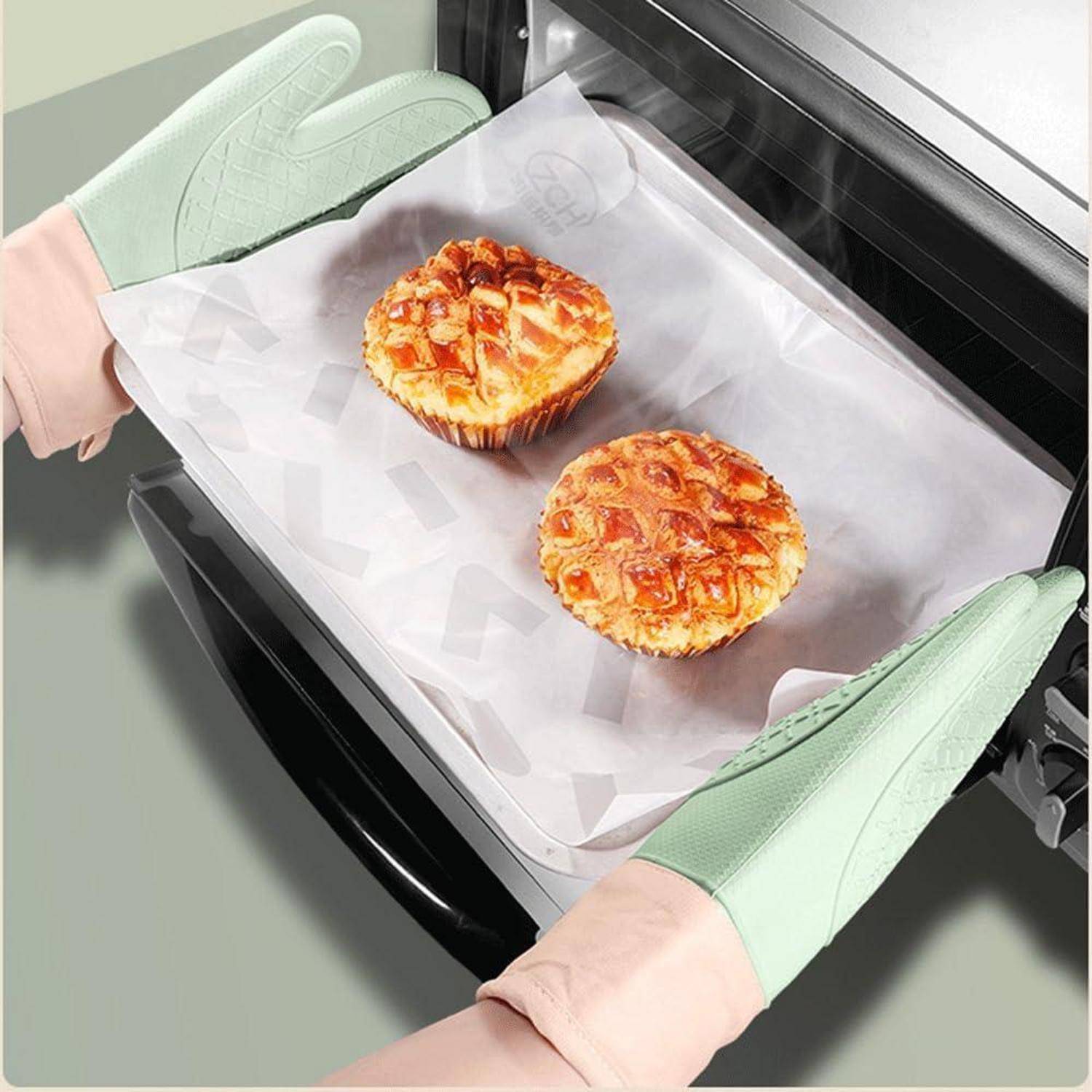 Zwei gebackene Muffins auf Pergamentpapier werden mit mintgrünen Ofenhandschuhen in einem Ofen gehalten.