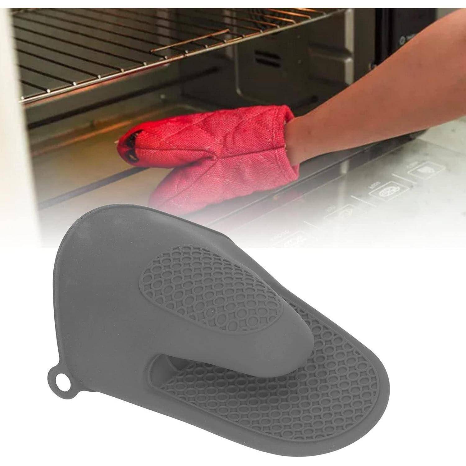 Schwarzer Silikon-Ofenhandschuh ruht vorne, mit einer Hand in einem roten Handschuh, die dahinter in einen Ofen greift.