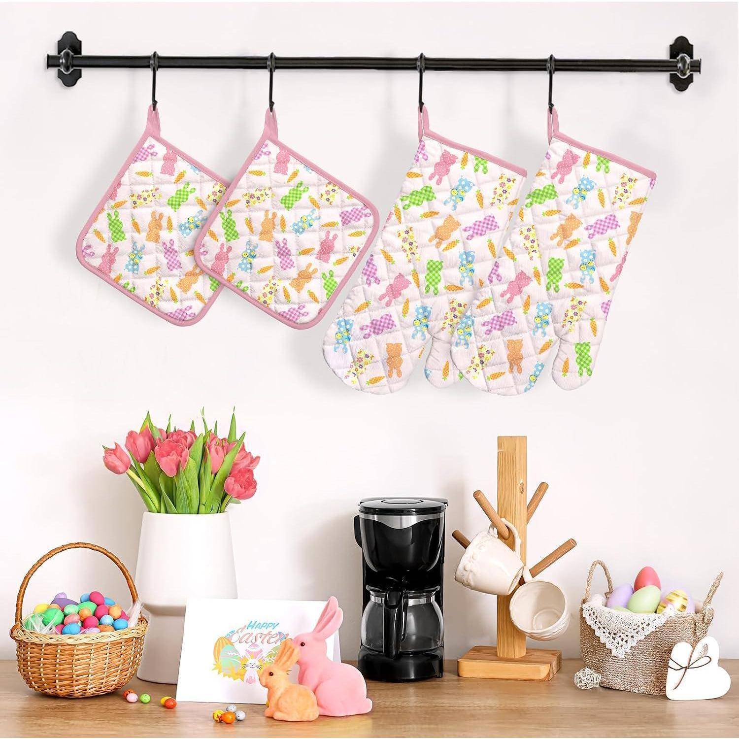 Küchendekor-Display mit pastellfarbenen, Ostern-inspirierten Ofenhandschuhen und Topflappen, die über einer Arbeitsplatte mit Kaffeemaschine, Tassen, Blumen und Körben mit Eiern hängen.