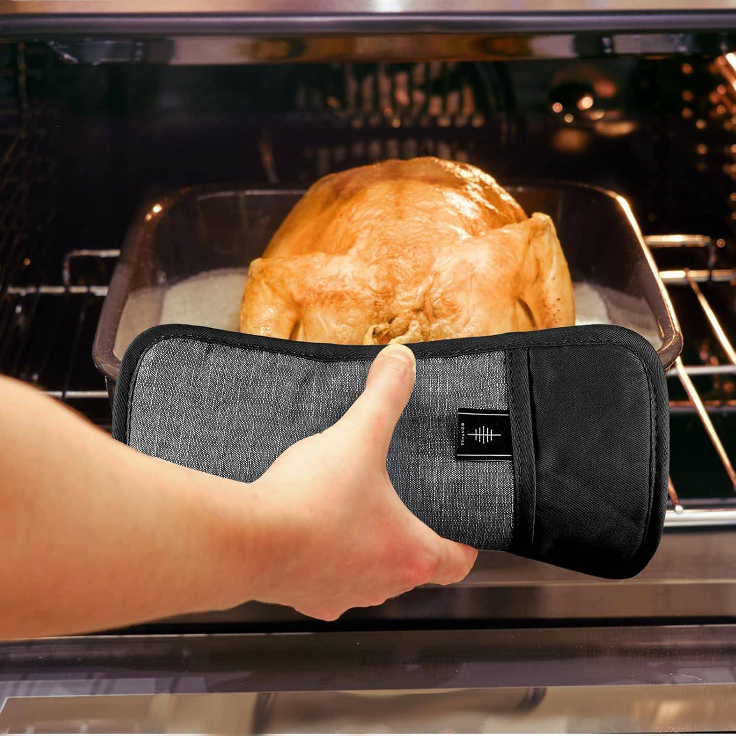 Hand, die einen gepolsterten Ofenhandschuh hält, vor einem Brathuhn im Ofen.