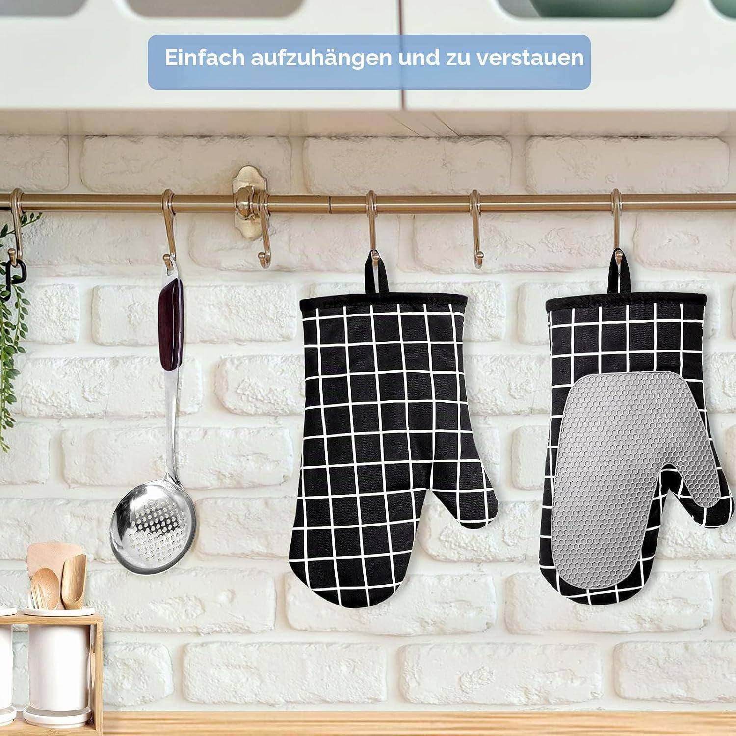 Zwei Ofenhandschuhe hängen an einer Wandschiene in einer Küche, neben einem Schaumlöffel und anderen Küchenutensilien, mit deutschem Text, der besagt „Einfach zum Aufhängen und Lagern