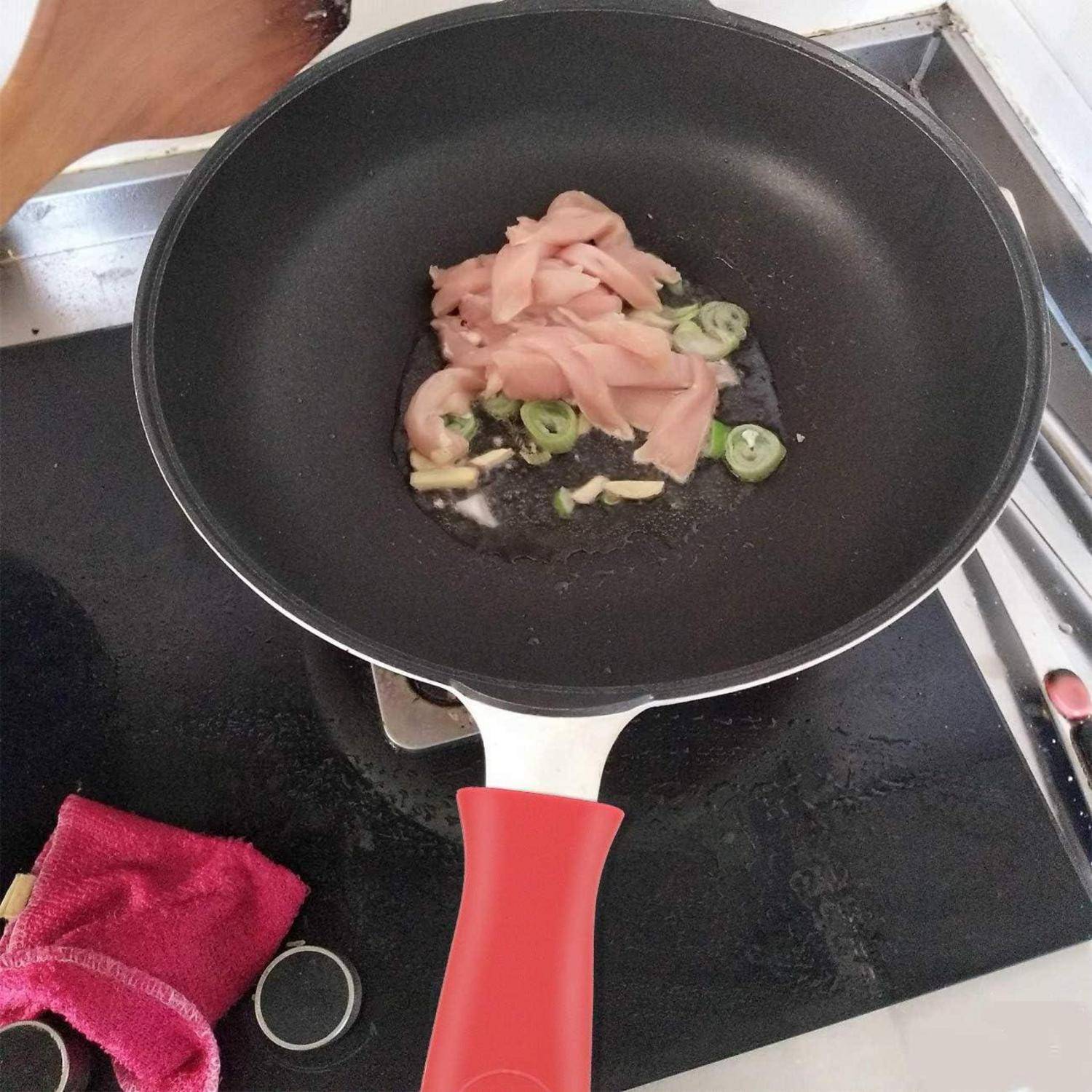 Geschnittenes Fleisch, Knoblauch und grüne Chilis kochen in einem schwarzen Wok auf einem Kochfeld, mit einem roten Griff und einem rosa Tuch in der Nähe.