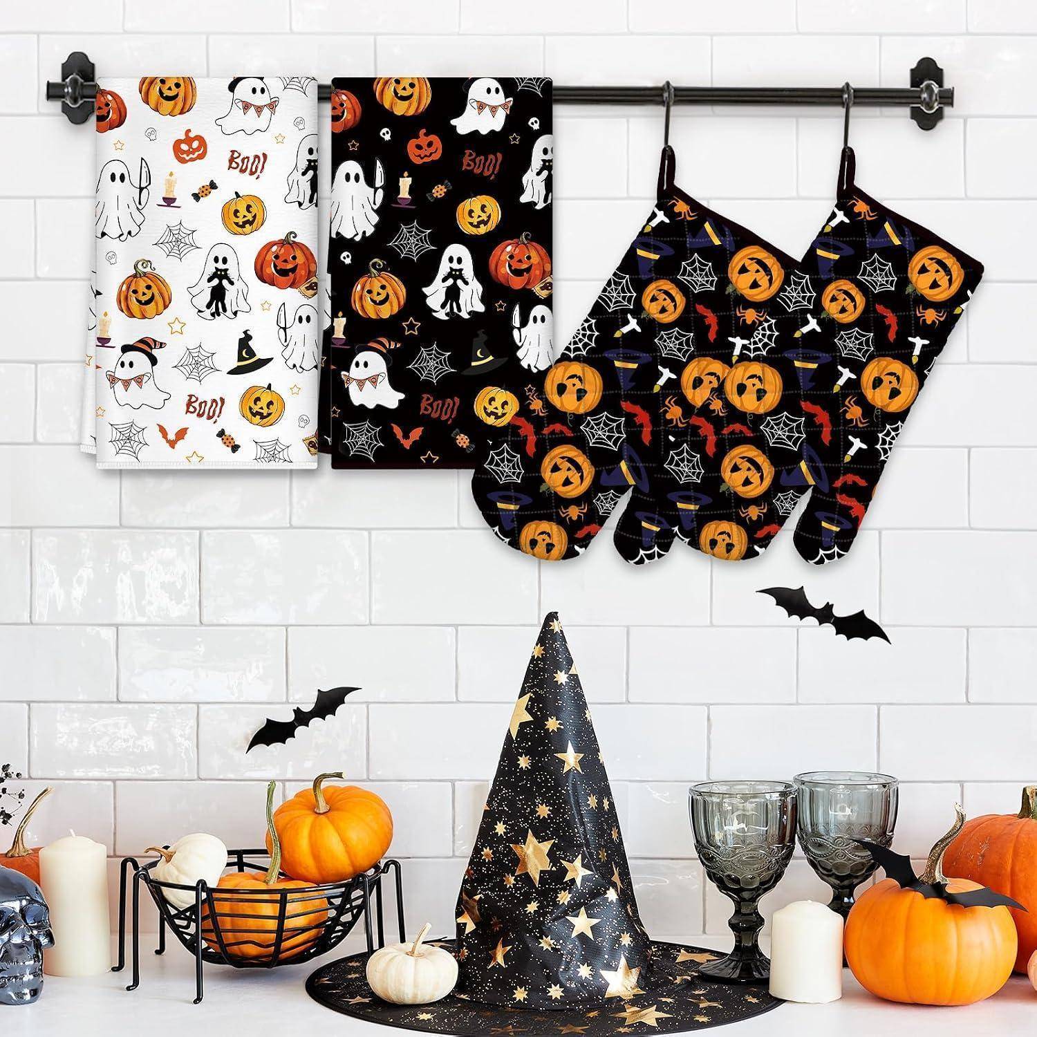 Halloween-Küchentext-Set mit Gespenst-, Kürbis-, Spinnennetz- und Fledermaus-Mustern: zwei Handtücher und drei Ofenhandschuhe auf einem Wandregal über saisonaler Dekoration.
