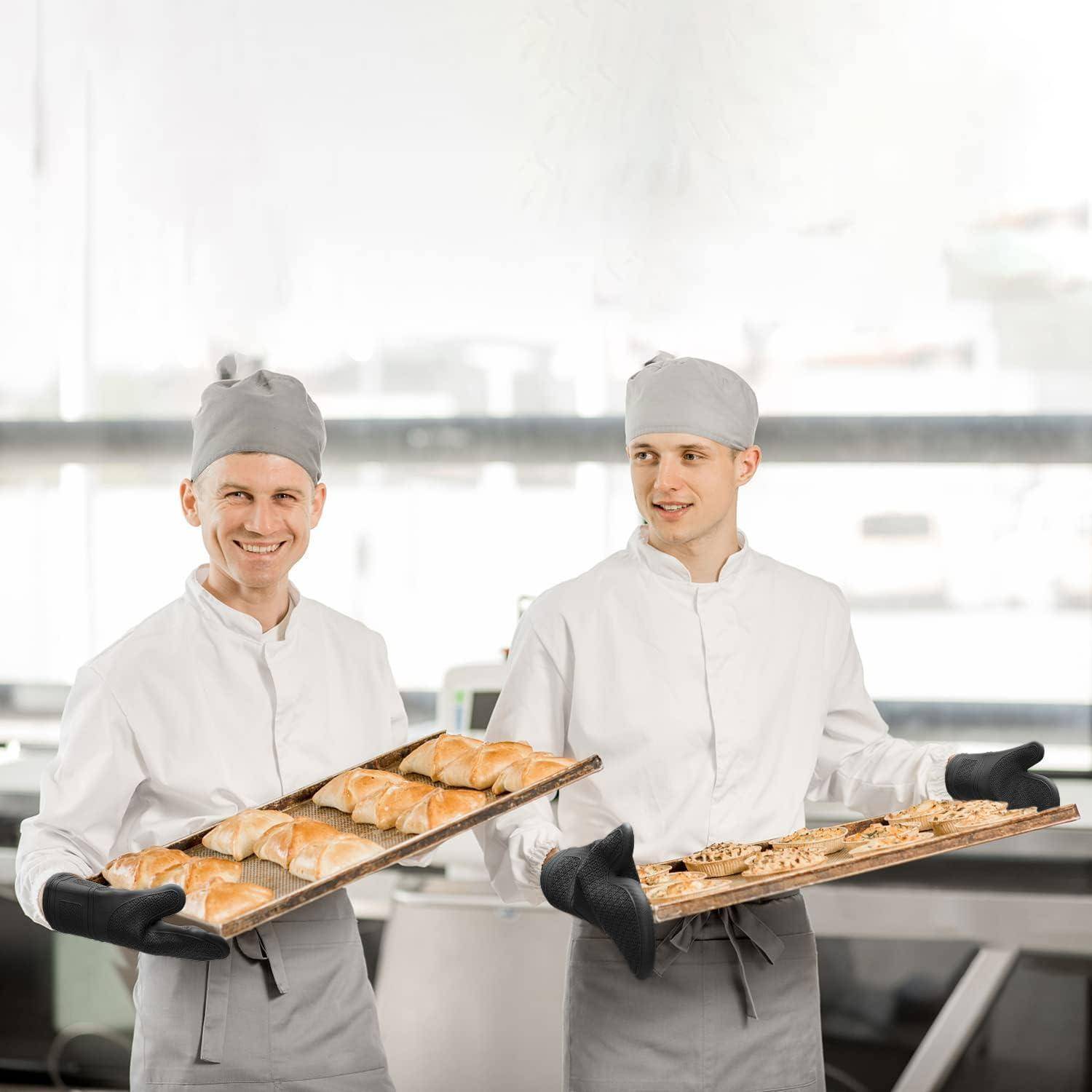 Zwei Bäcker in weißen Uniformen und grauen Mützen halten Tabletts mit frisch gebackenem Brot in einer hellen Bäckerei-Küche.