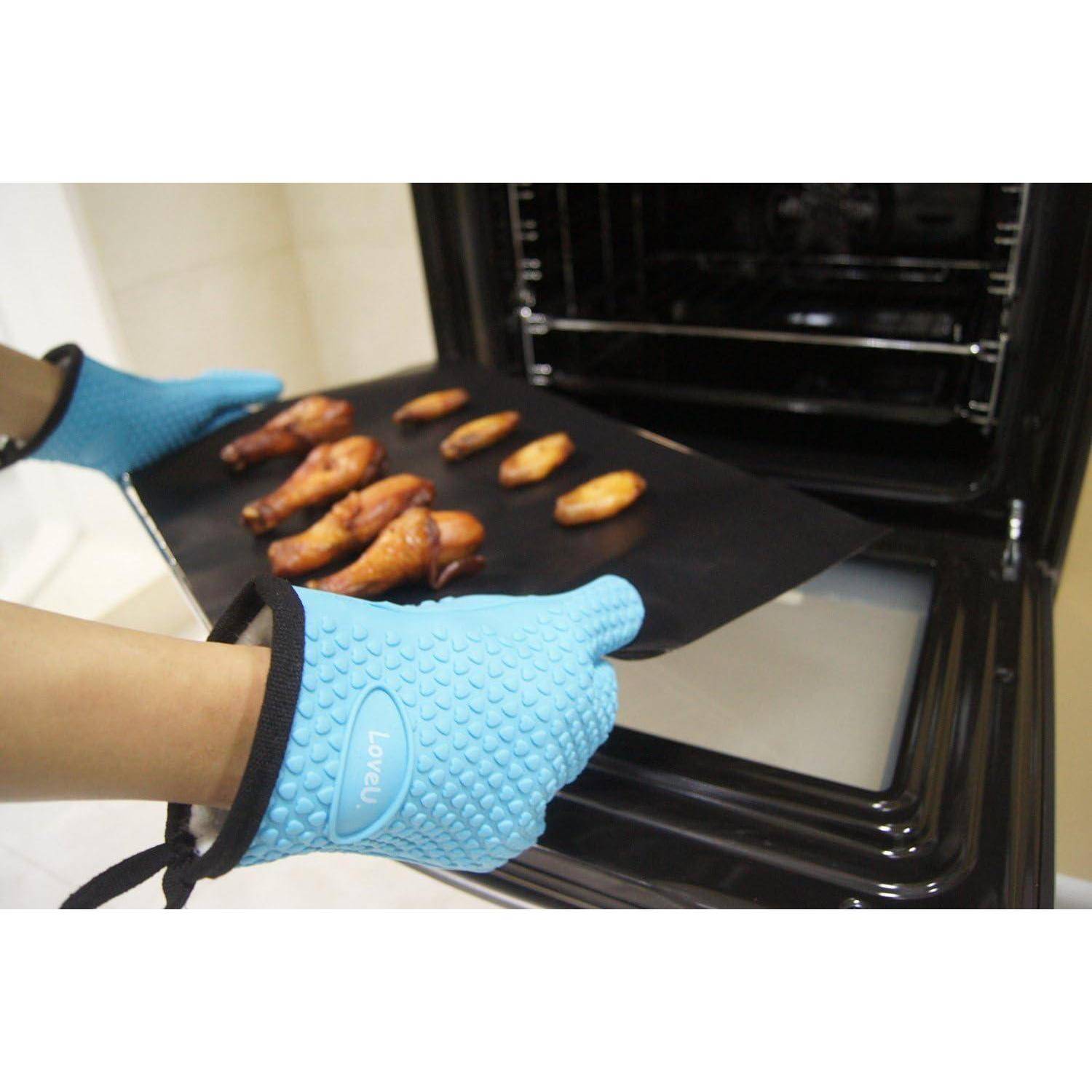 Blaue Ofenhandschuhe halten ein Tablett mit gekochten Hähnchenschenkeln, das aus einem Ofen entnommen wird.