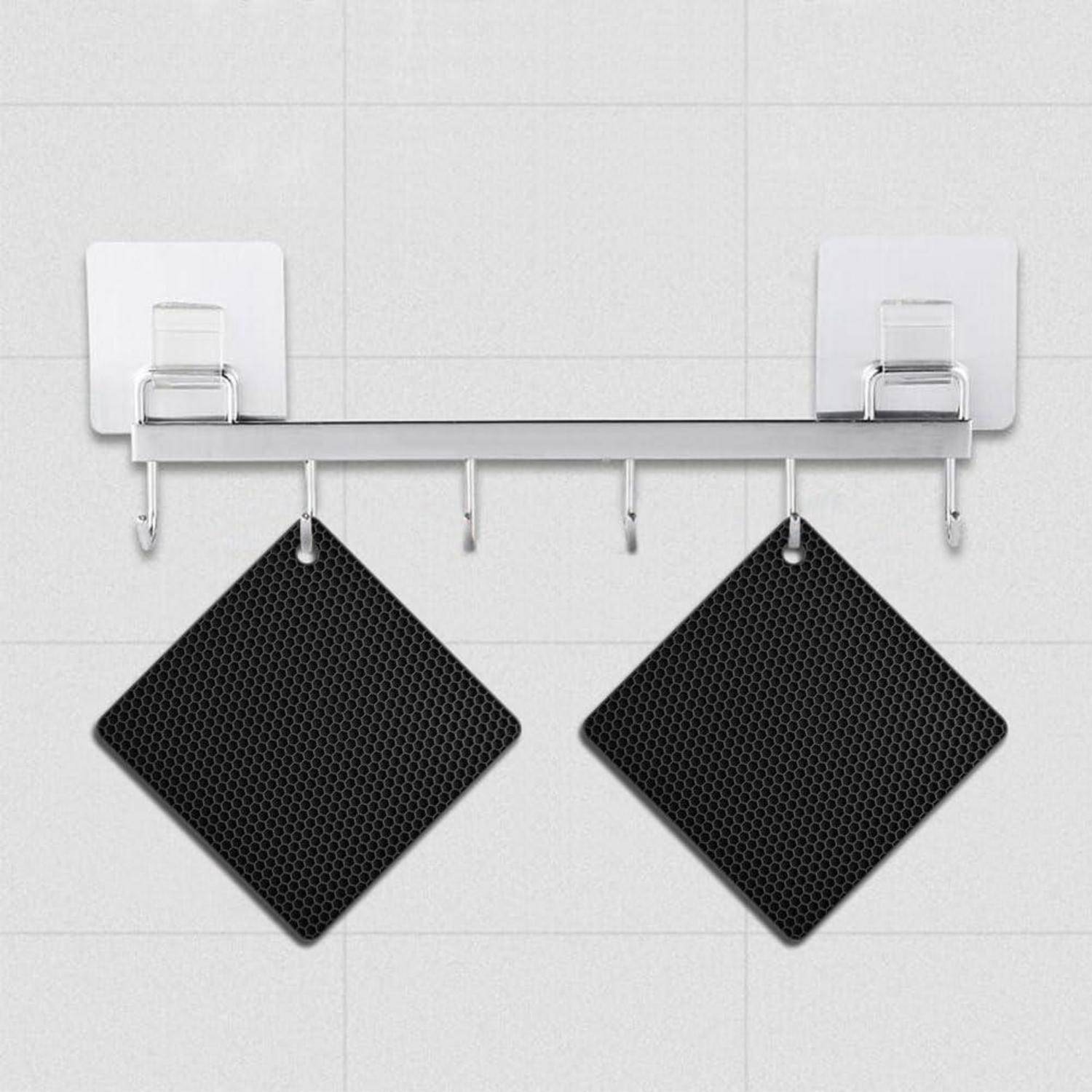 Wandmontiertes Metallregal mit Haken, an denen zwei schwarze, diamantförmige Reinigungspads oder Handtücher an einer gekachelten Wand hängen.