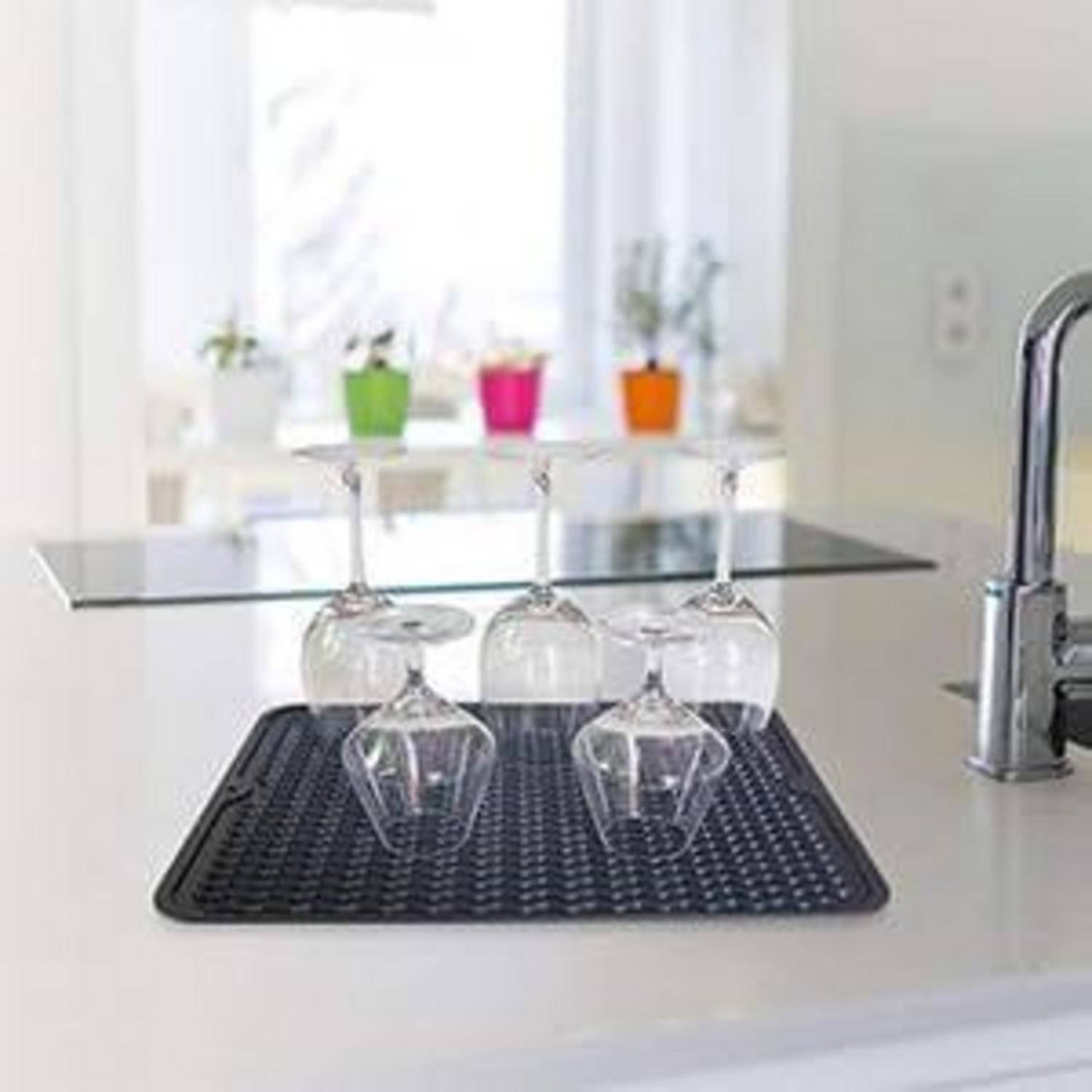 Umgestülpte Weingläser und ein Trinkglas, die auf einer schwarzen Matte neben einem Wasserhahn in einer hellen modernen Küche trocknen.