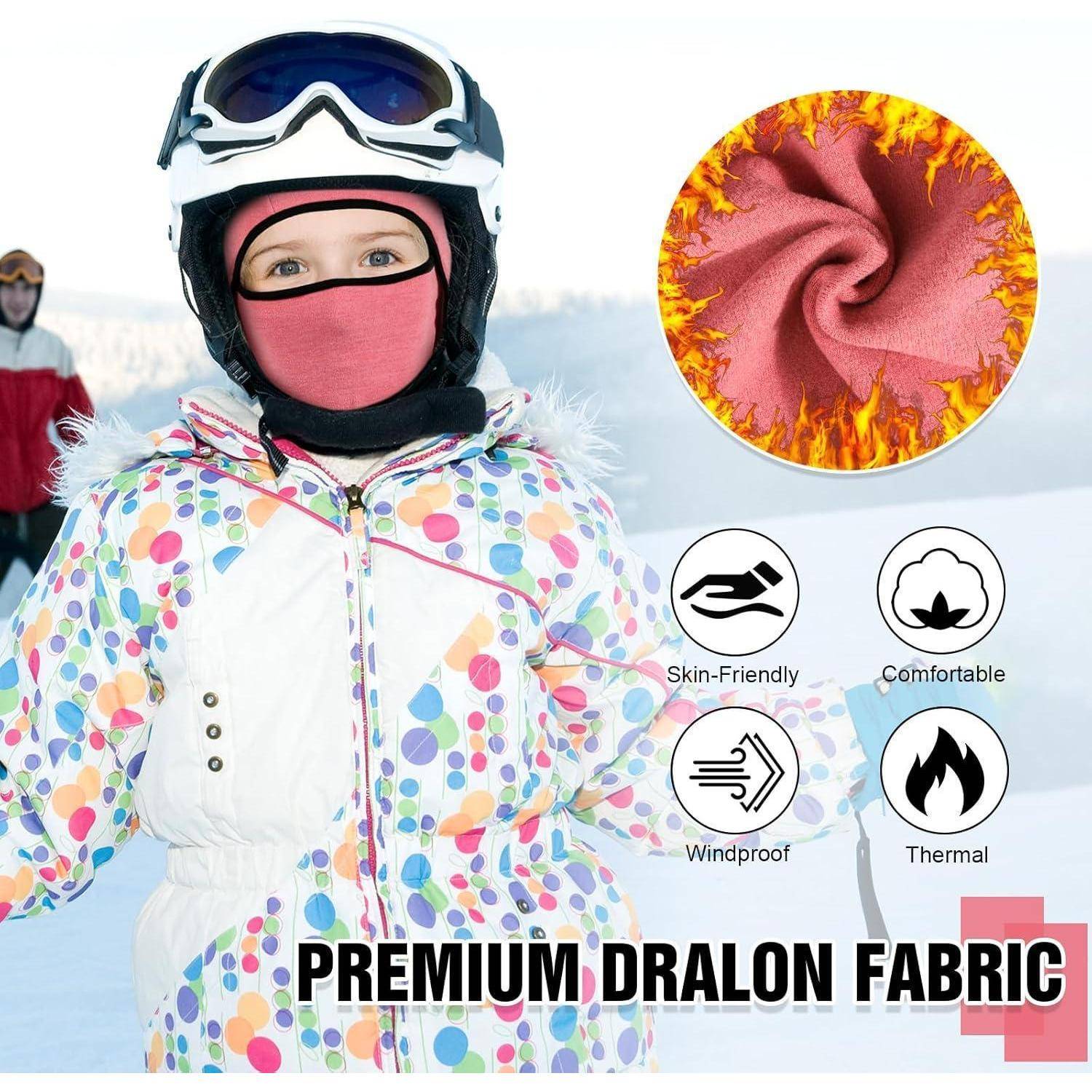 Kind in Winterskiausrüstung mit rosa Gesichtsbedeckung und gemusterter Jacke, mit Symbolen, die „Hautfreundlich", „Komfortabel"", „Winddicht"" und „Wärmend"" premium Dralon-Stoff bewerben.