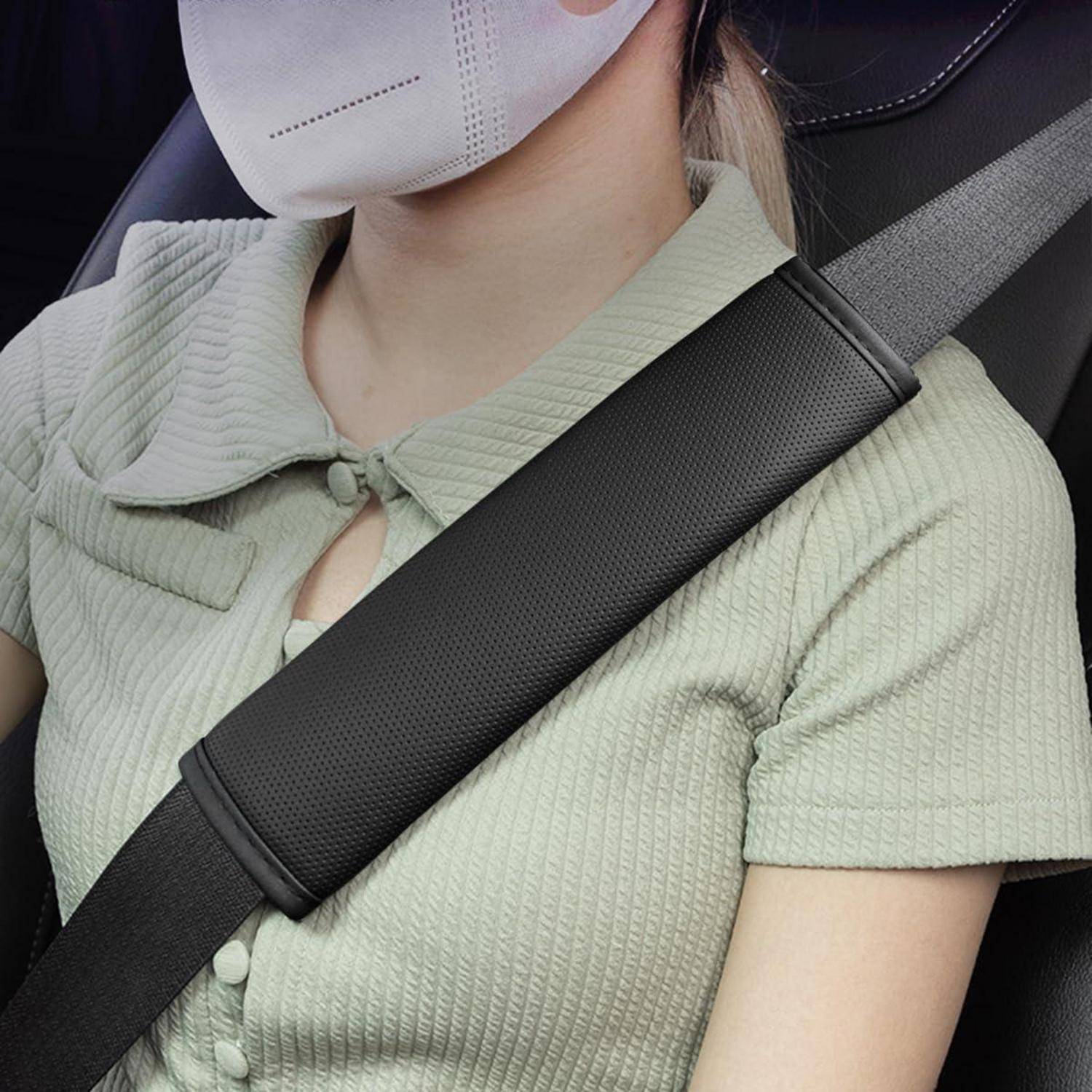 Person mit weißer Maske und mintgrünem Oberteil mit angelegtem schwarzem Sicherheitsgurt über der Brust im Auto.