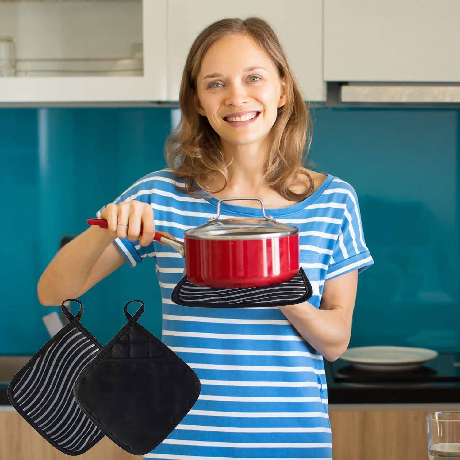 Lächelnde Frau in einer Küche, die einen roten Topf mit Ofenhandschuhen hält, was auf Kochen oder Essenszubereitung hindeutet.
