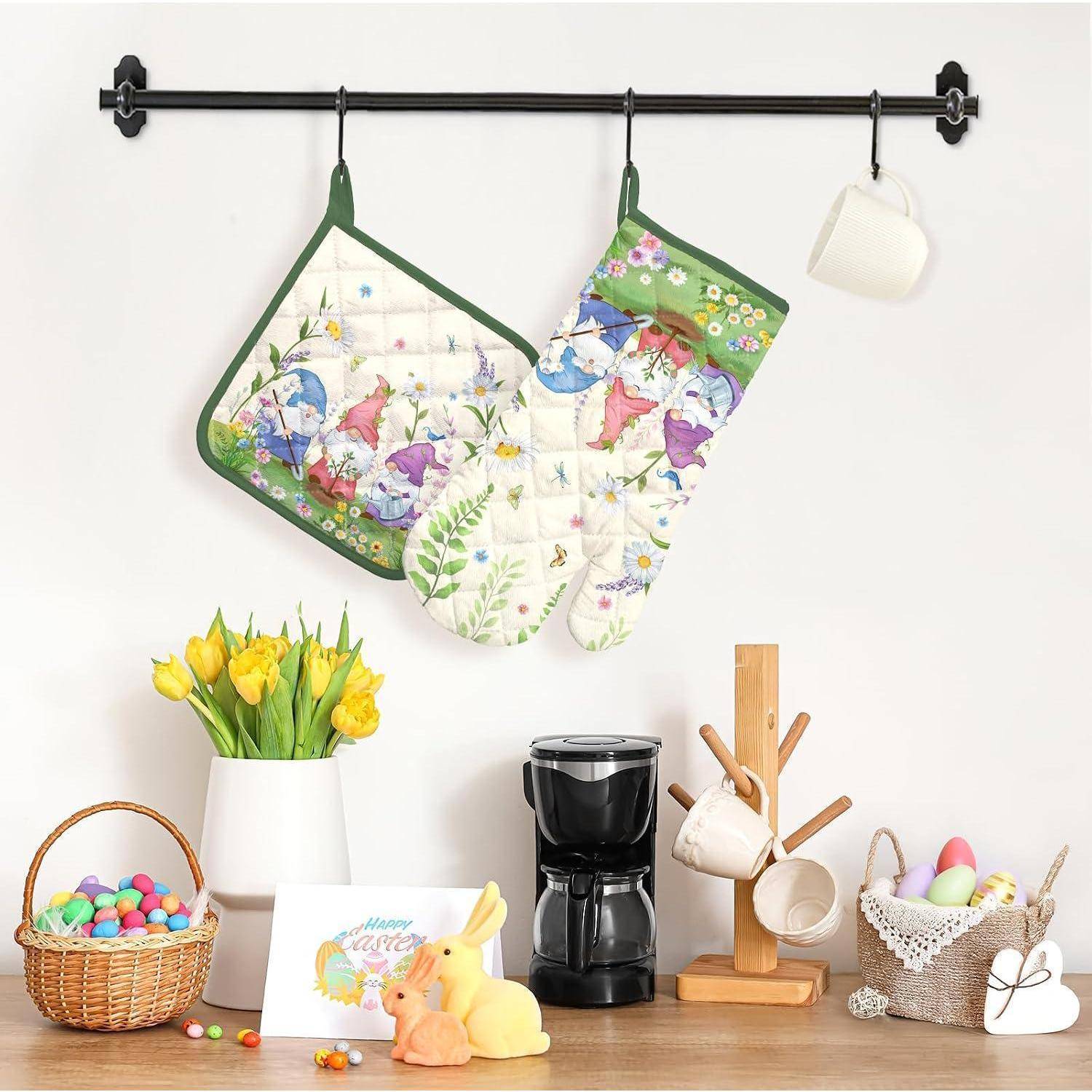 Küchenwandregal mit zwei floralen Ofenhandschuhen und einer weißen Tasse über einer Arbeitsplatte mit Osterdeko, einer Kaffeemaschine, Blumen und Geschirrzzubehör.