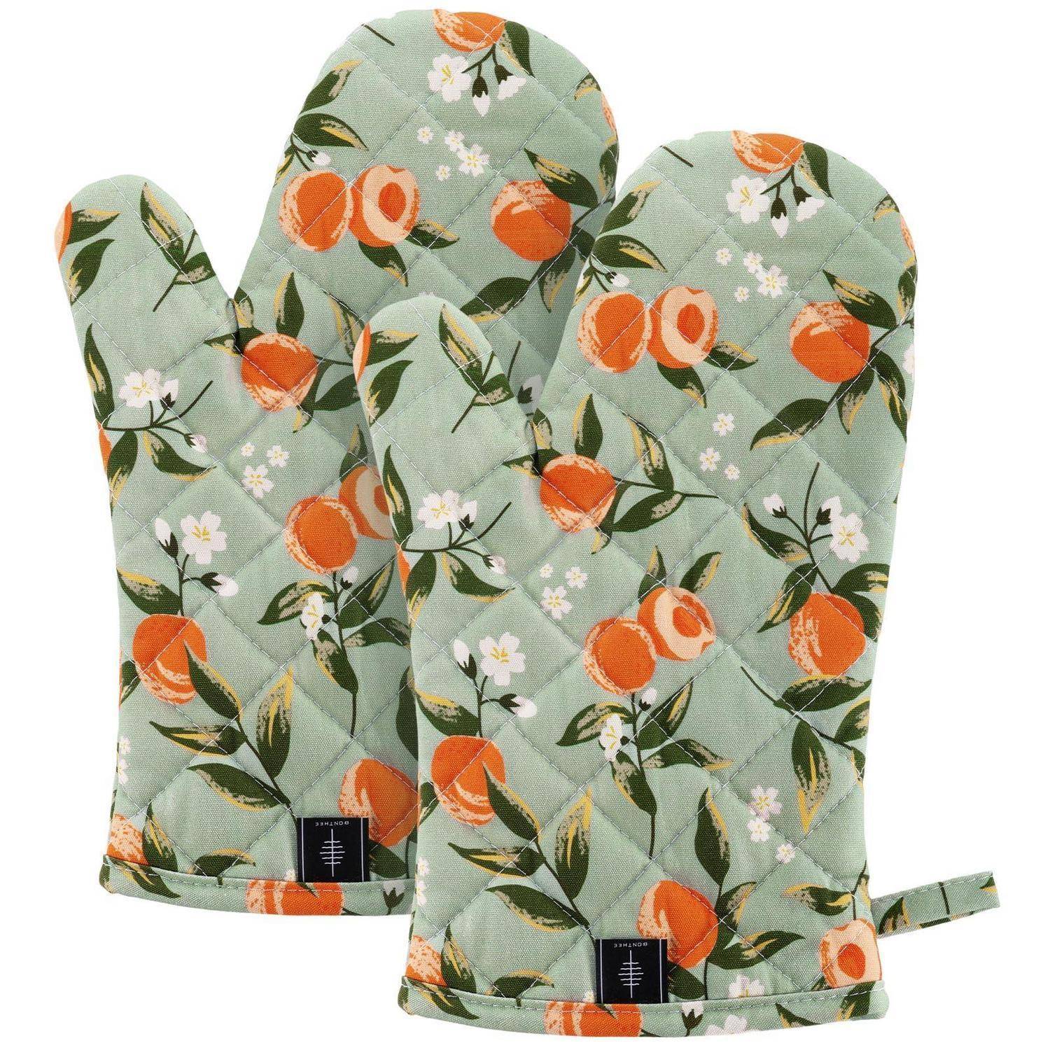 Paar gesteppter Ofenhandschuhe mit mintgrünem Stoff und orangefarbenem Obst- und Blumenmuster auf weißem Hintergrund.