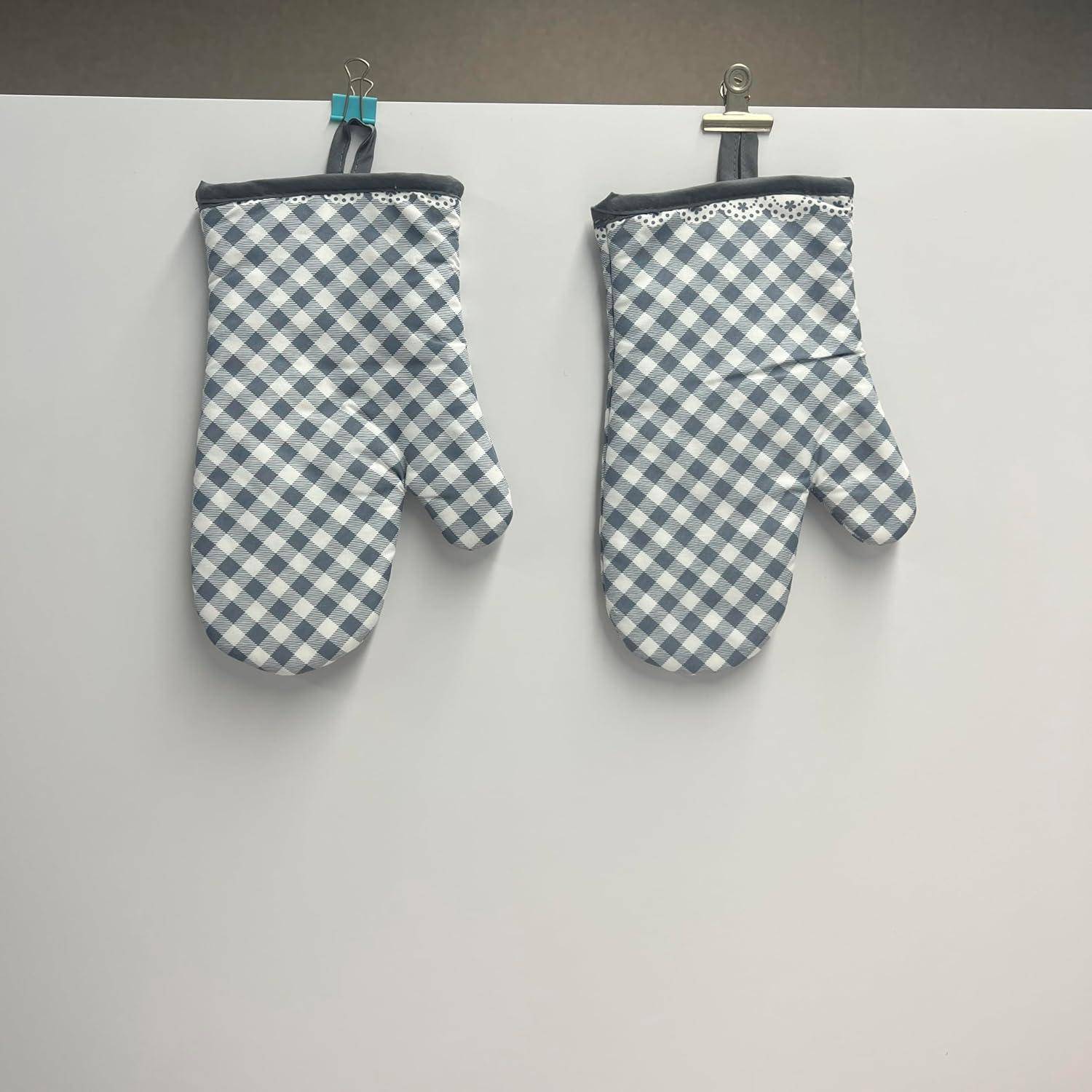 Zwei blau-weiß karierte Ofenhandschuhe an einer weißen Wand befestigt, einer mit Spitzeneinsatz, nebeneinander hängend.