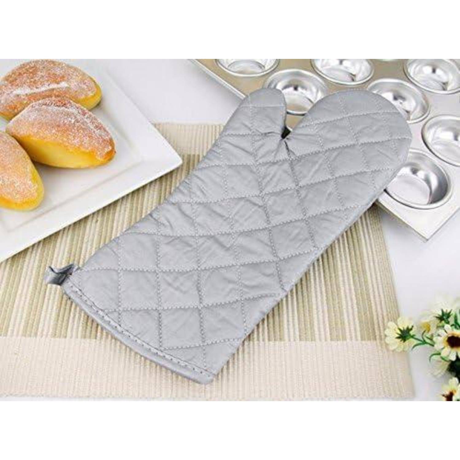 Grauer gesteppter Ofenhandschuh auf einem Tisch neben gebackenen Brötchen und Muffinformen, was auf Küchenbäckerei und Wärmeschutz hindeutet.