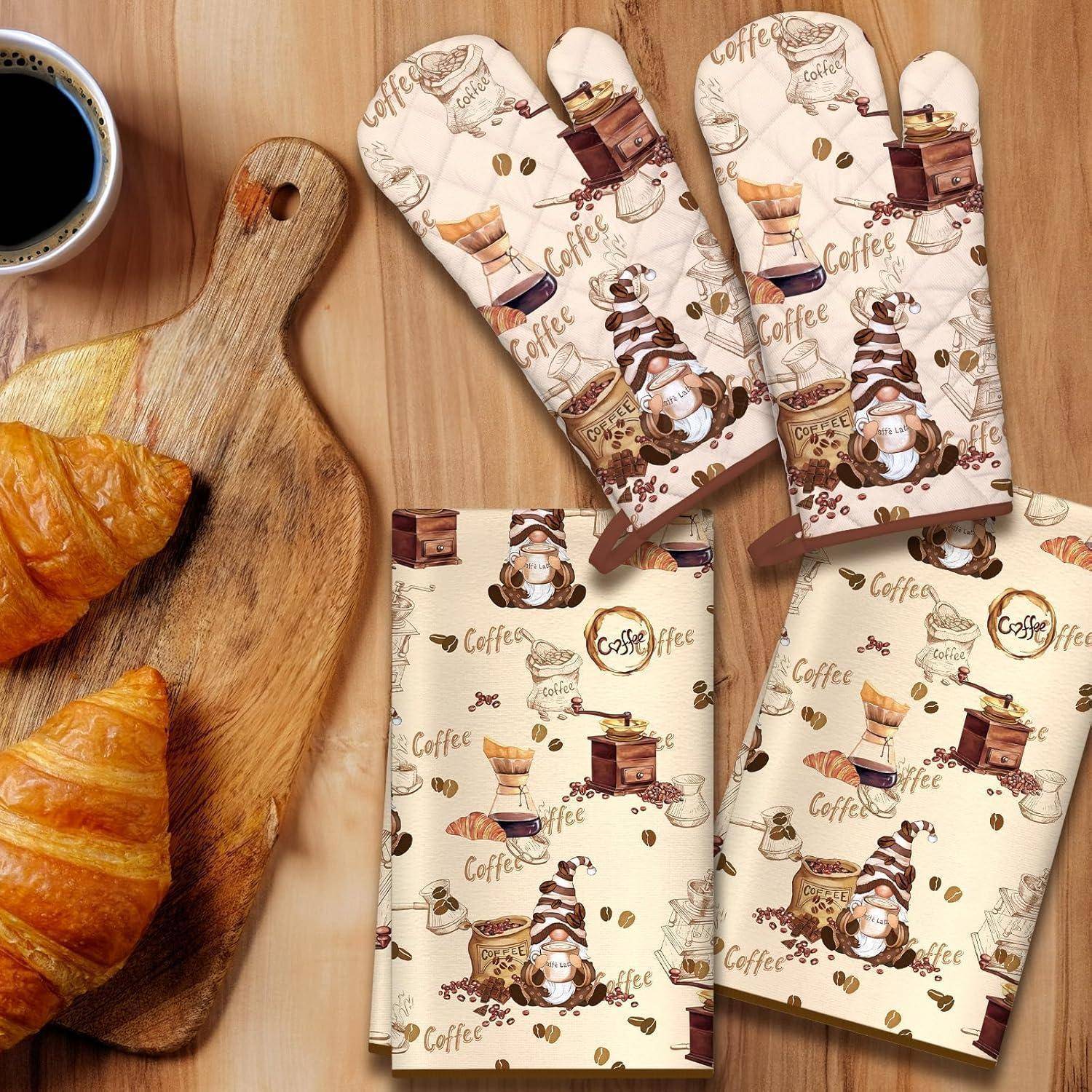 Kaffee-Themen-Ofenhandschuhe aus Stoff und passende Servietten, neben einem Croissant und einer Tasse Kaffee auf einem Holzbrett angezeigt.
