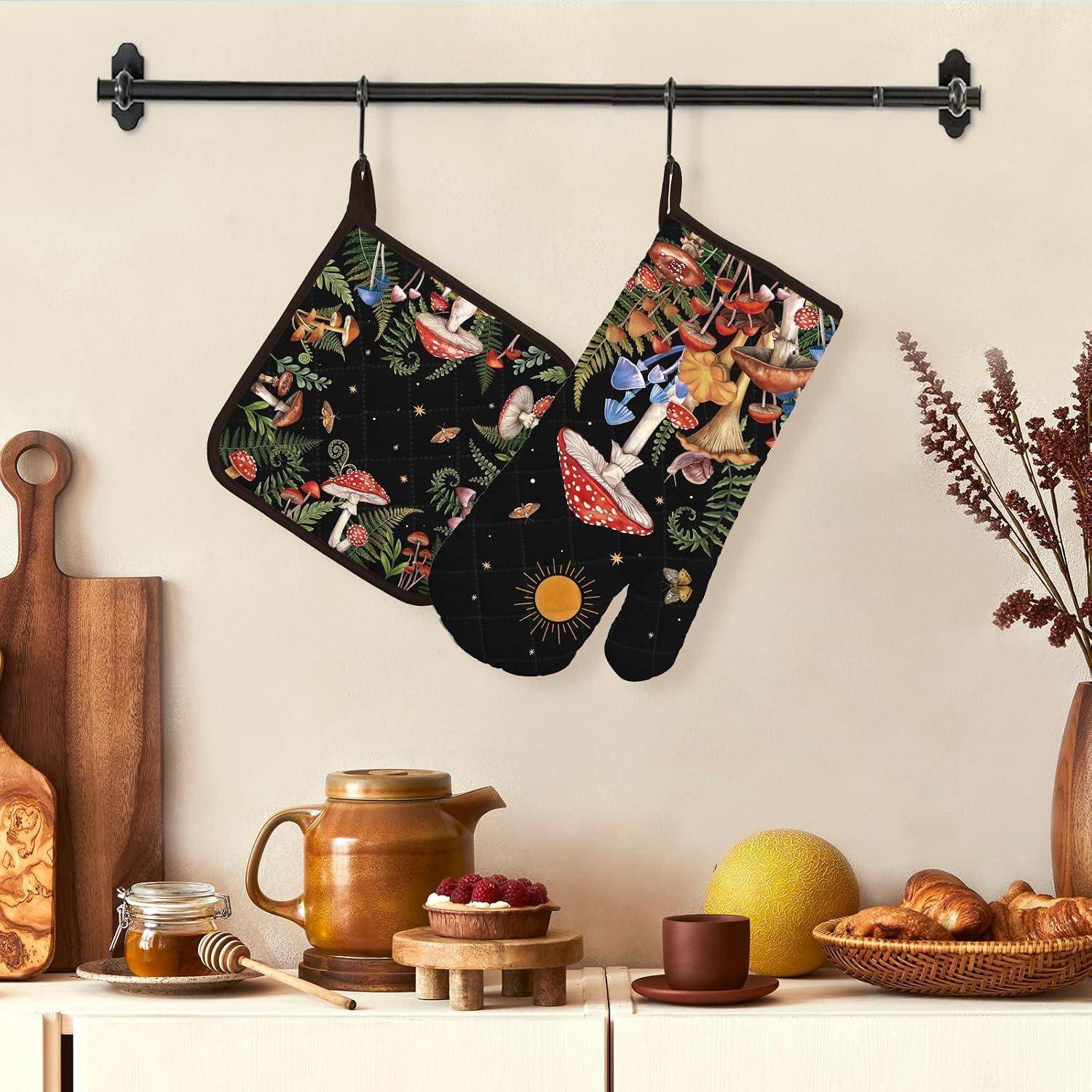 Zwei gemusterte Ofenhandschuhe hängen auf einer Wandleiste über einer stilisierten Küchentheke mit Honig, einem Kupferkrug, Obst und Brot.