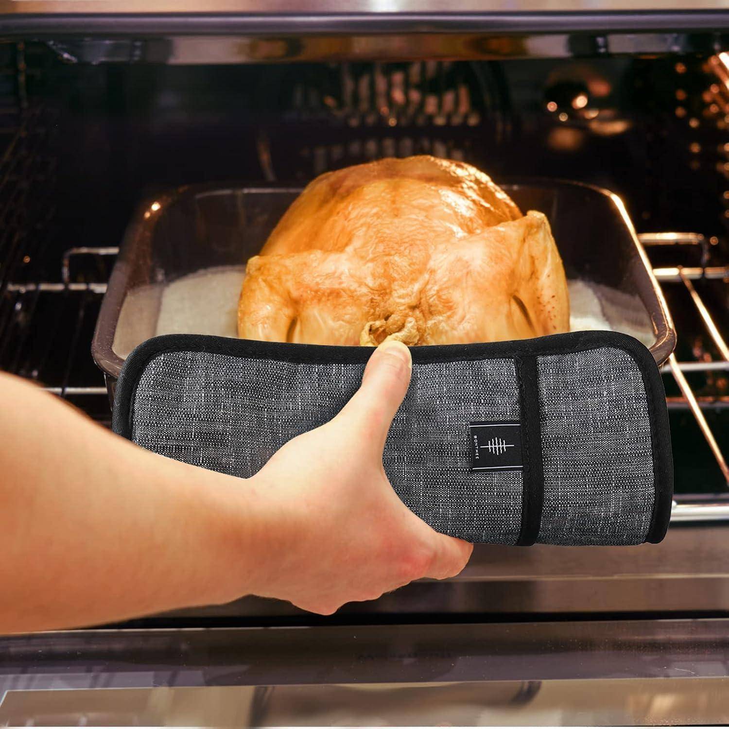 Eine Hand mit einem Ofenhandschuh zieht eine Bratpfanne mit einem gebratenen Hähnchen aus einem Ofen.