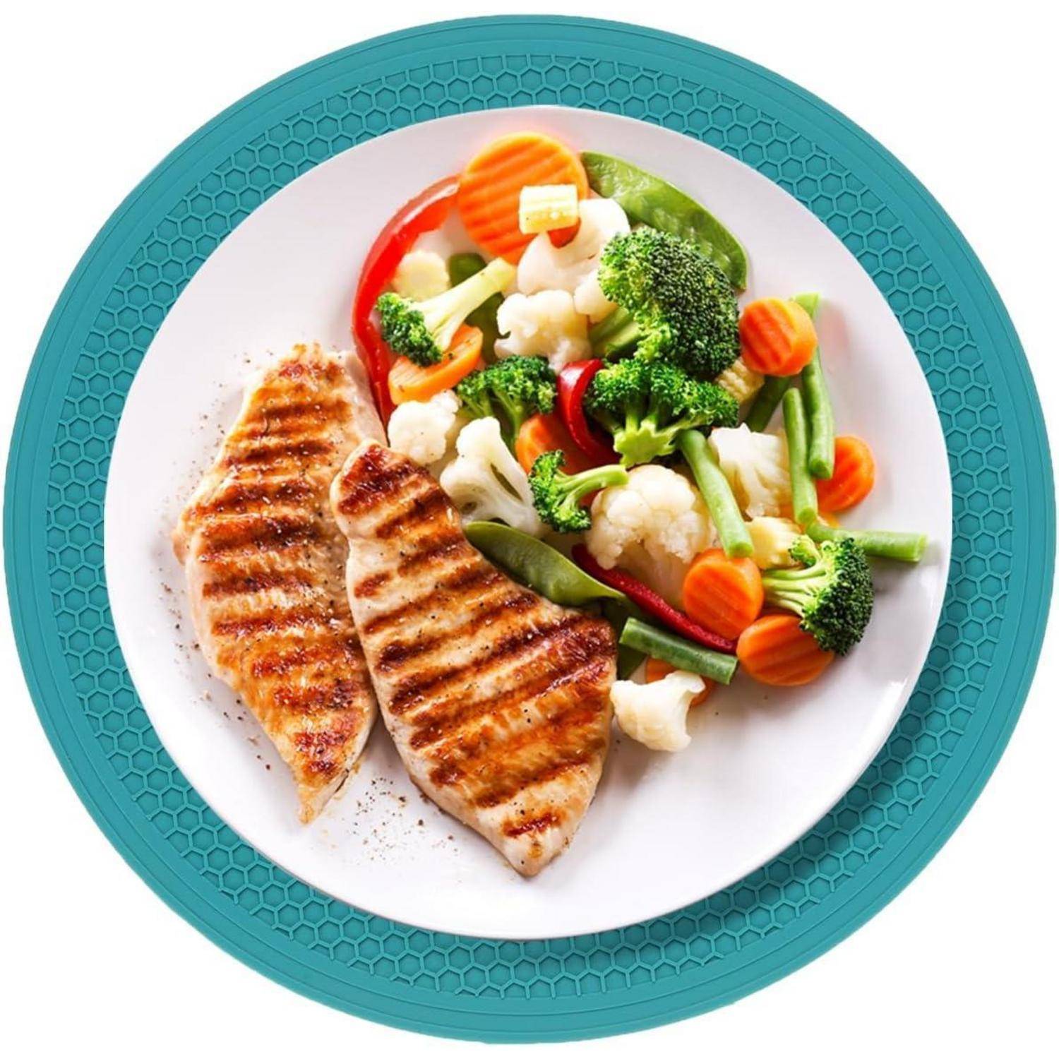Gegrillte Hähnchenbrust mit gedünstetem Gemüsemix auf einem weißen Teller mit einer türkisen Tischunterlage.