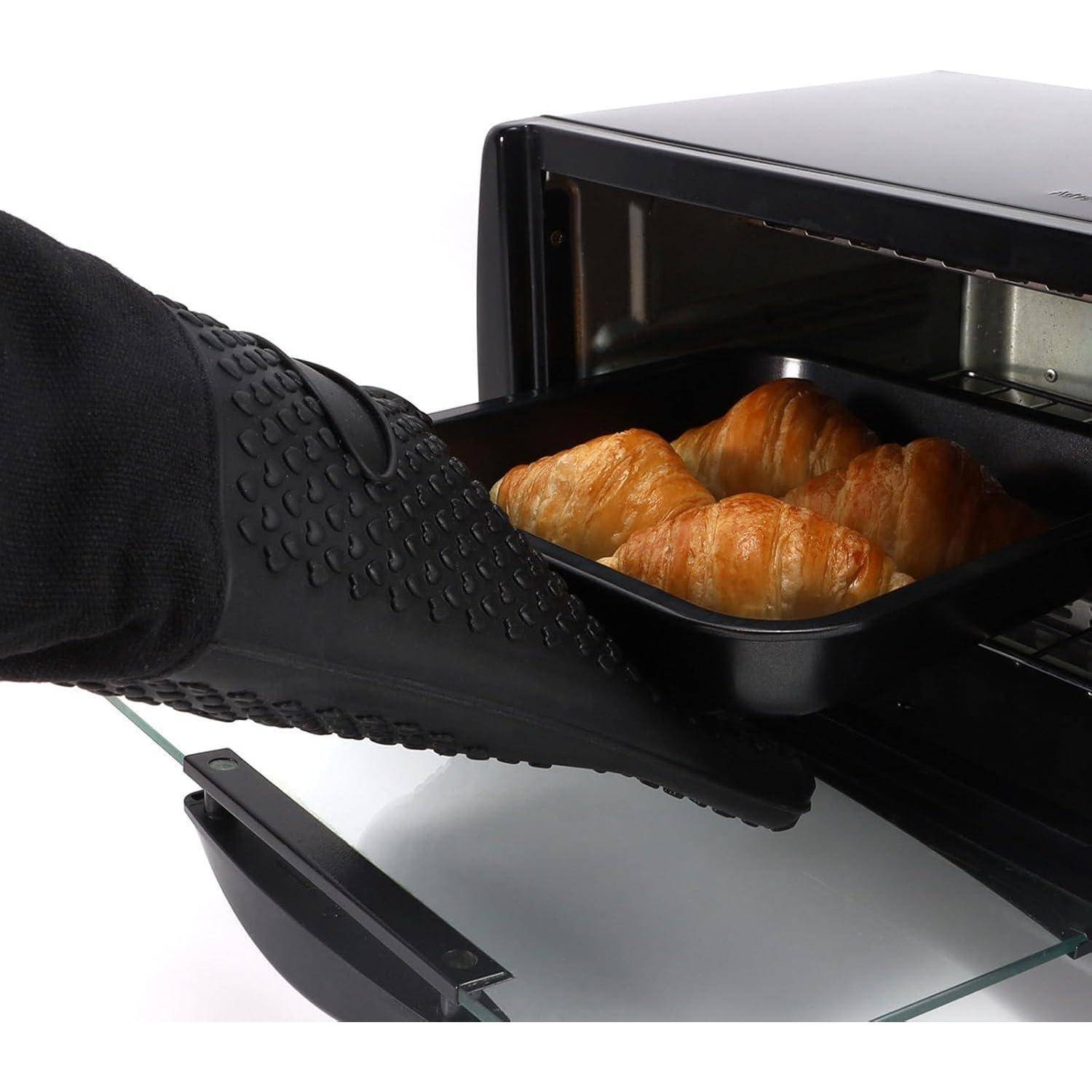 Schwarzer Ofenhandschuh hält ein Tablett mit Croissants, das aus einem kleinen Ofen herausgenommen wird.