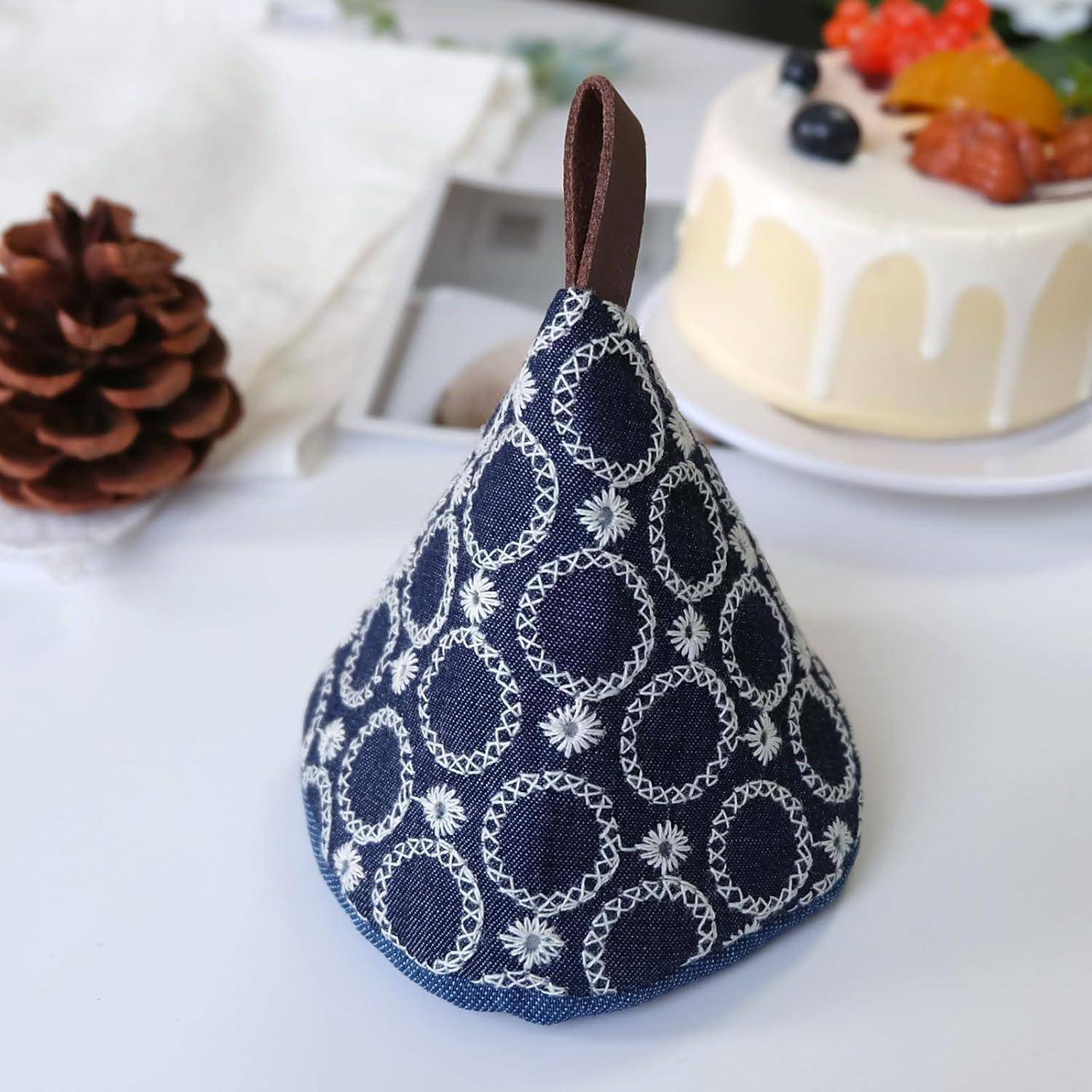 Beutel mit Kordelzug aus blauem gemustertem Stoff mit brauner Schleifenhenkel, auf einem Tisch neben einem Kuchen und einer Tannenzapfen platziert.