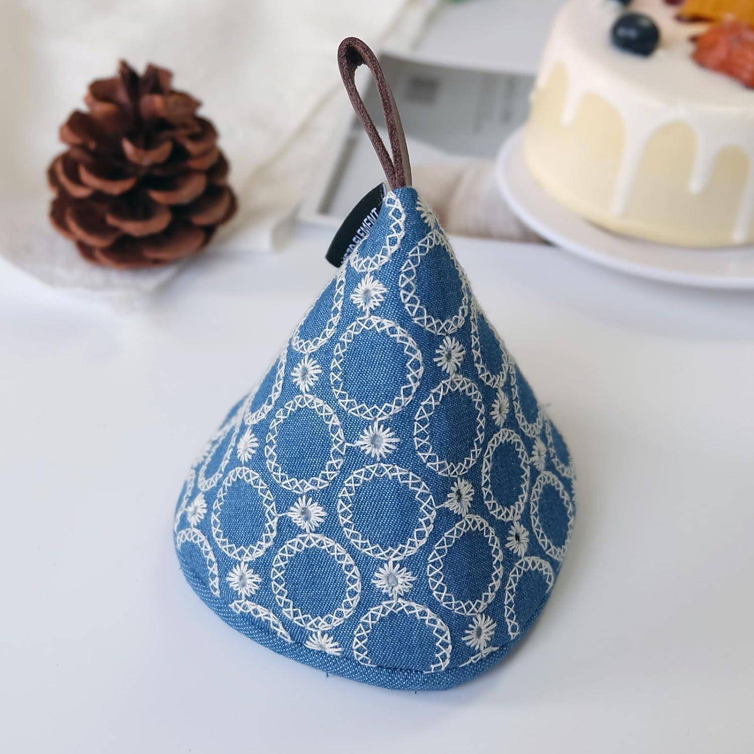Blaugemusterter Stoff-Türstopper oder Gewicht mit Griffschlaufe, stehend auf einer weißen Oberfläche mit einer unscharfen Tannenzapfen und einem Kuchen im Hintergrund.