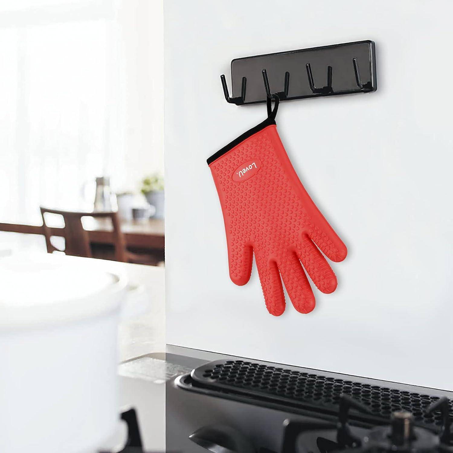 Rote, hitzebeständige Silikonhandschuh, der an einem schwarzen, wandmontierten Haken in einer Küche neben einem Kochfeld hängt.