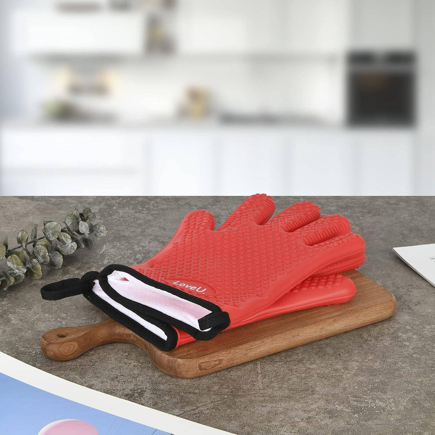 Roter Silikon-Ofenhandschuh mit schwarzweißem Bündchen liegt auf einem Holzschneidebrett in einer Küchenumgebung.