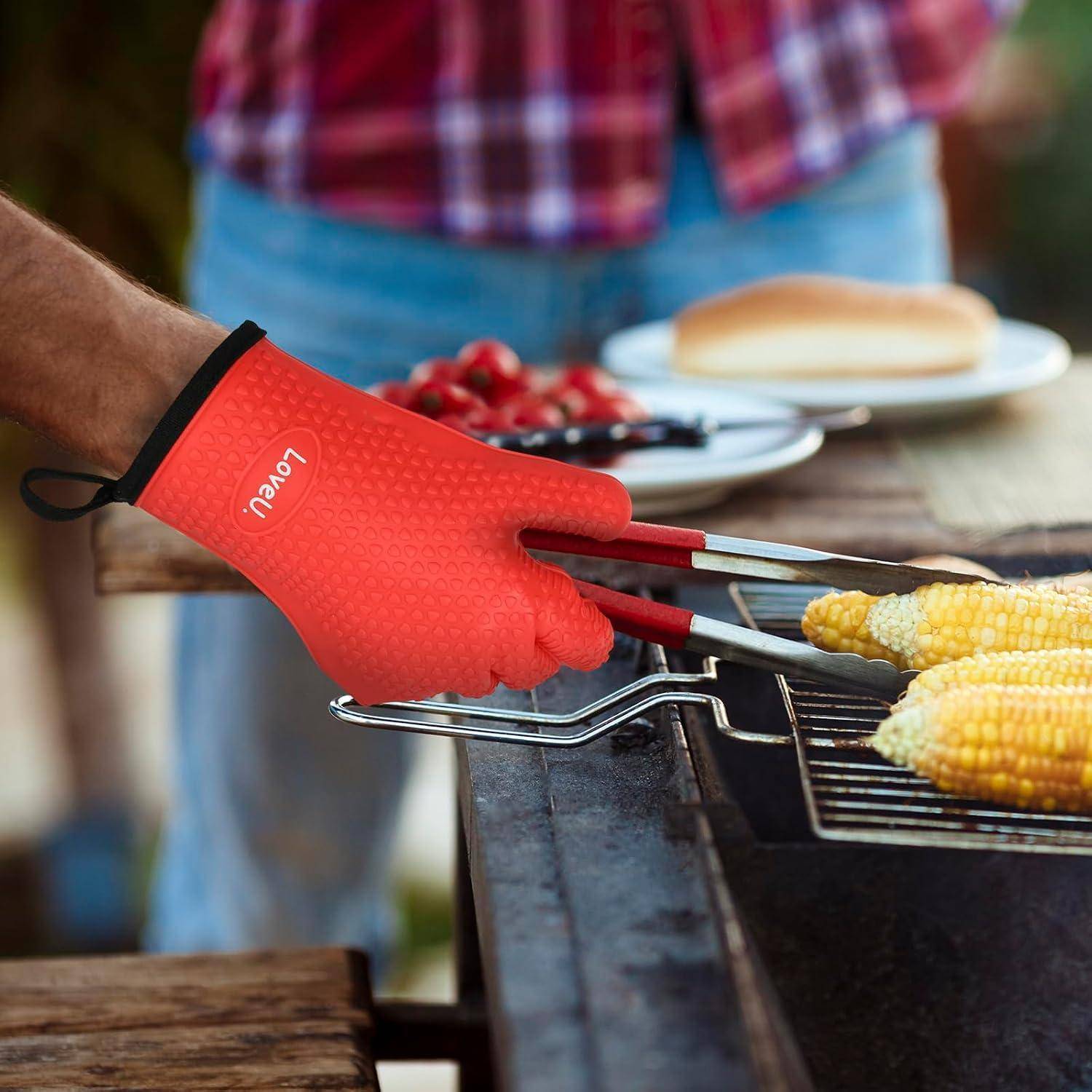 Person trägt einen roten hitzebeständigen Grillhandschuh und benutzt Zangen, um Mais auf einem Barbecue-Grill zu wenden.