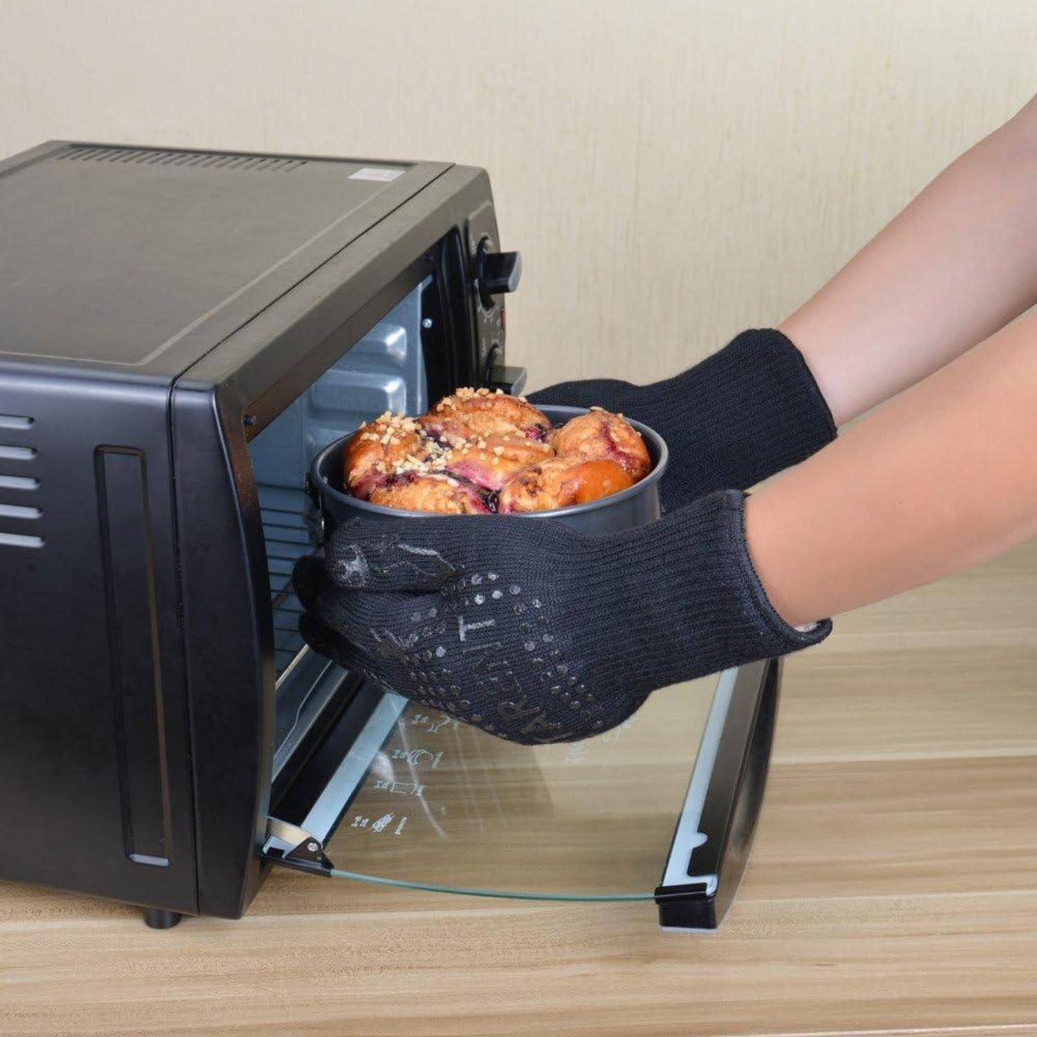 Eine Person mit schwarzen Ofenhandschuhen stellt eine Schüssel mit gebackenem Essen in einen Toasterofen auf der Arbeitsplatte.