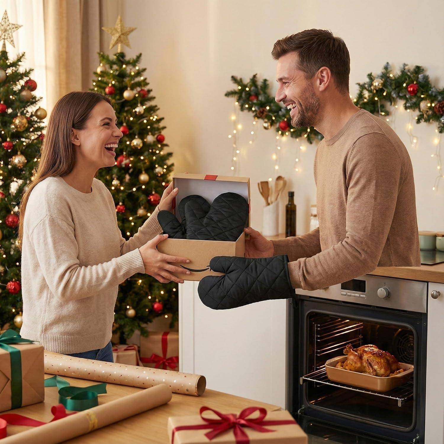 Ein lächelndes Paar tauscht eine Geschenkbox in einer dekorierten Küche mit Weihnachtsbäumen, Geschenken und einem Braten aus, der im Ofen gart.