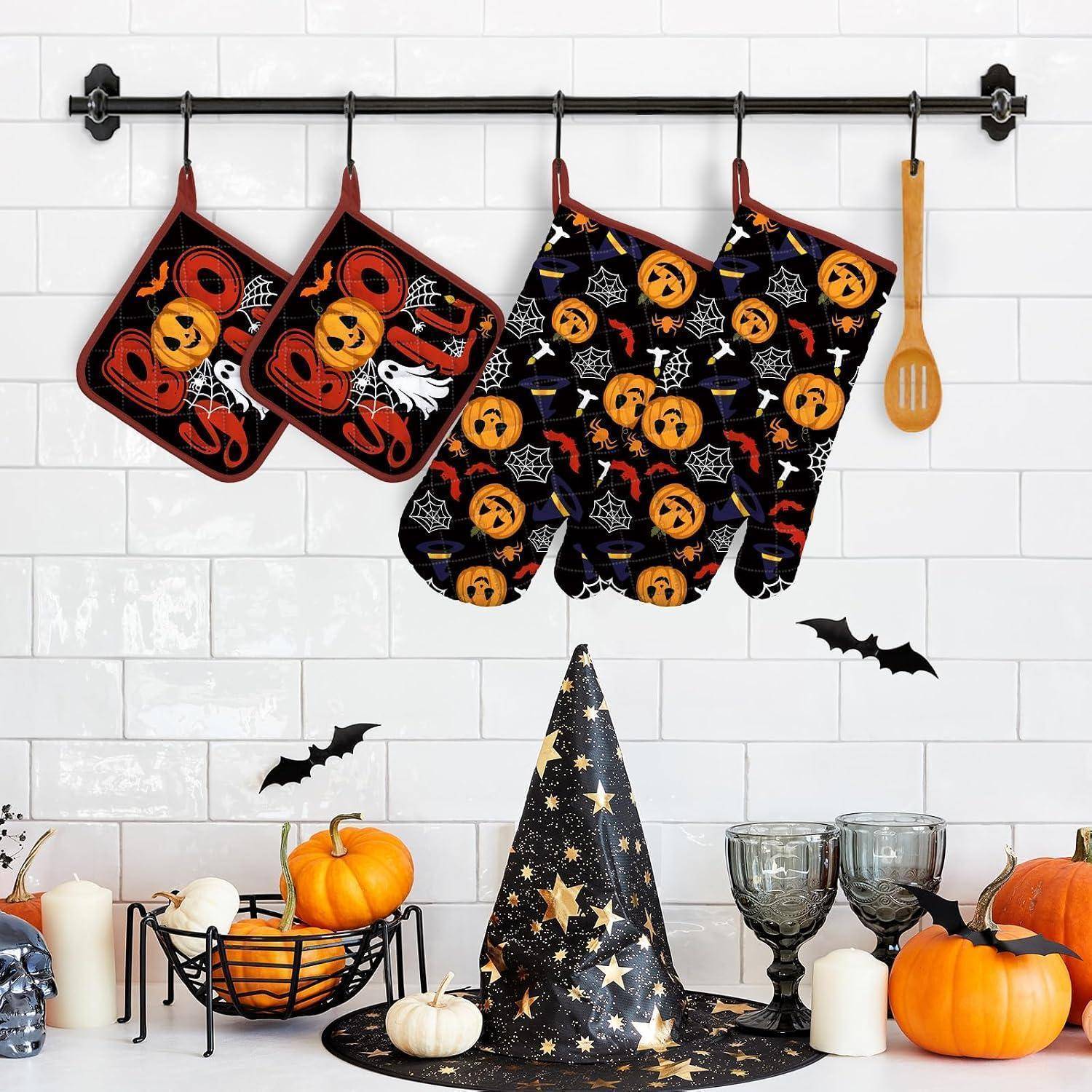 Halloween-Küchendekor mit kürbismustrigen Ofenhandschuhen und sternenbesetztem Spitzhut, die über einer Theke mit Kürbissen, Kerzen, Fledermäusen und Kelchen hängen.