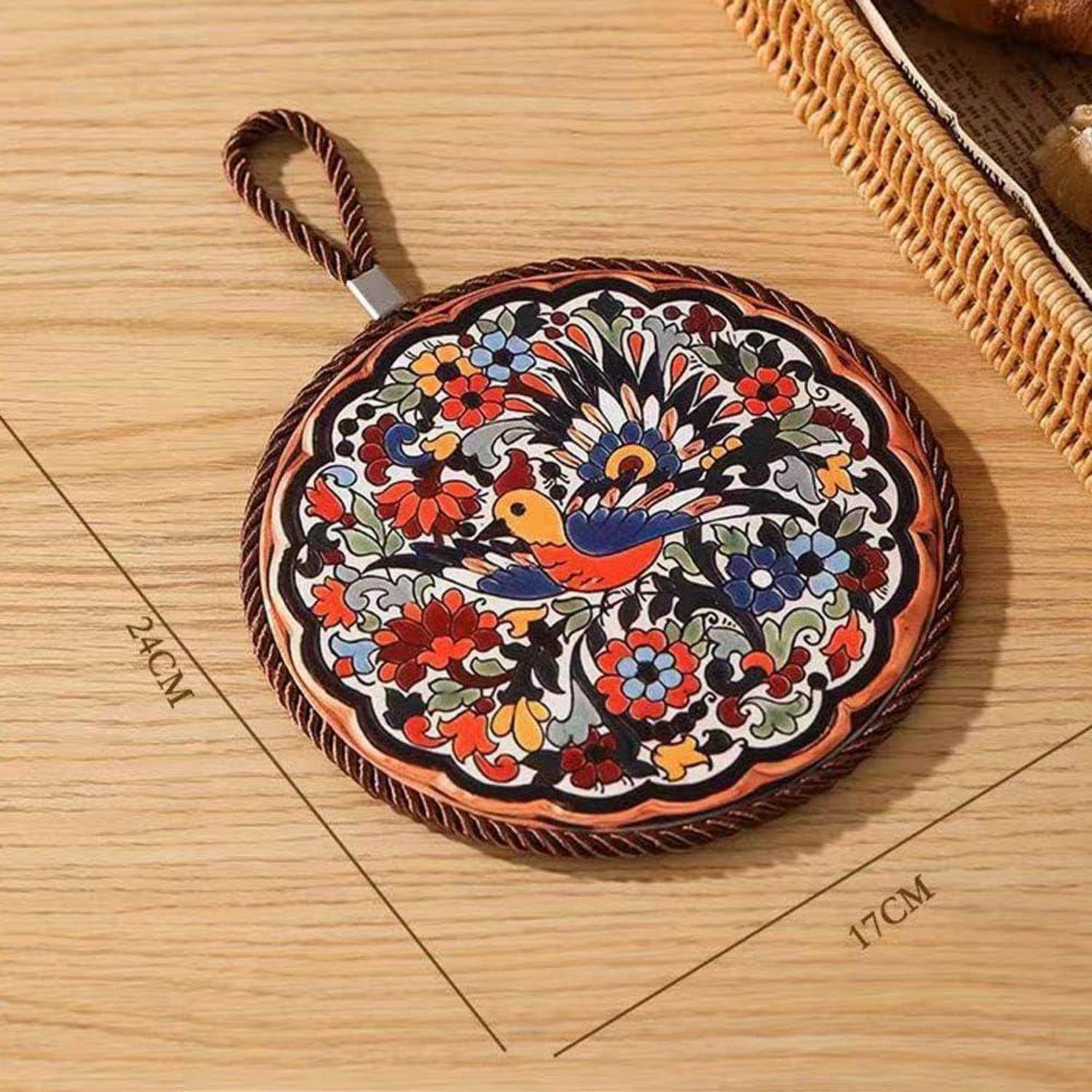 Rundes Blumen-Untersetzer oder Topflappen mit Schleifengriff, mit einem bunten Vogel- und Blumenmuster auf einer Holzoberfläche mit Markierungen von 24 cm und 17 cm.