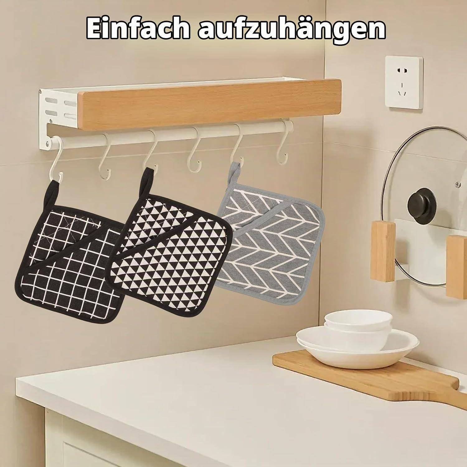 Wandmontierte Holzleiste mit Haken, an denen drei hängende Ofenhandschuhe oder Topflappen über einer Küchenarbeitsplatte hängen; deutscher Text lautet „Einfach aufzuhängen