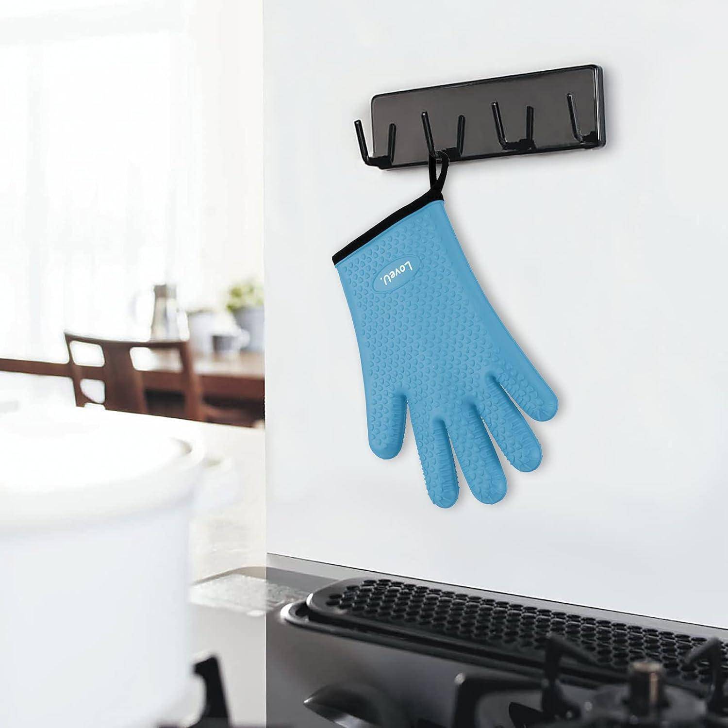 Blauer Silikonhandschuh für den Ofen, der an einer wandmontierten schwarzen Hakenleiste in einer Küche hängt.