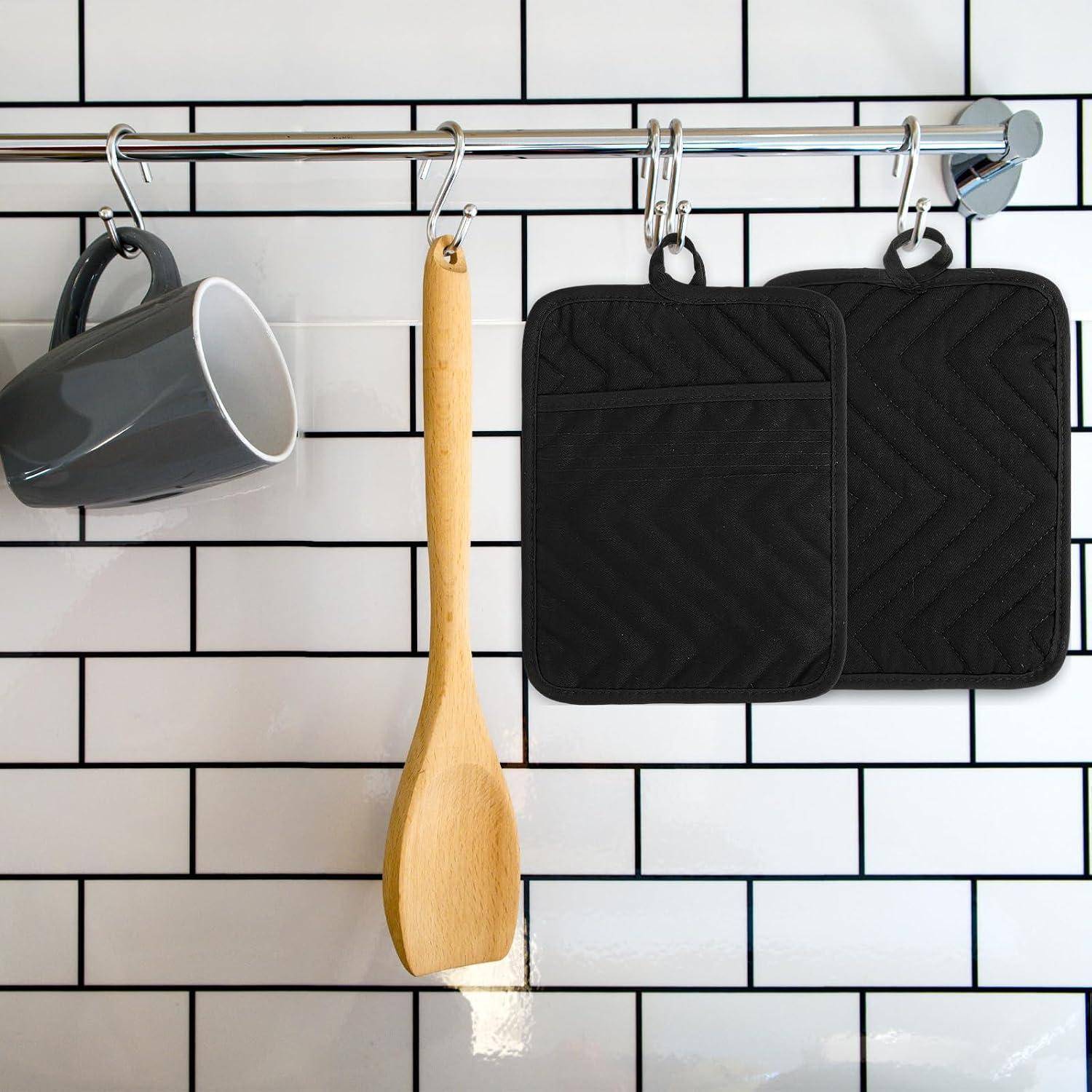 Küchenleiste mit hängender grauer Tasse, Holzlöffel und zwei schwarzen Ofenhandschuhen an einer weiß gefliesten Wand.