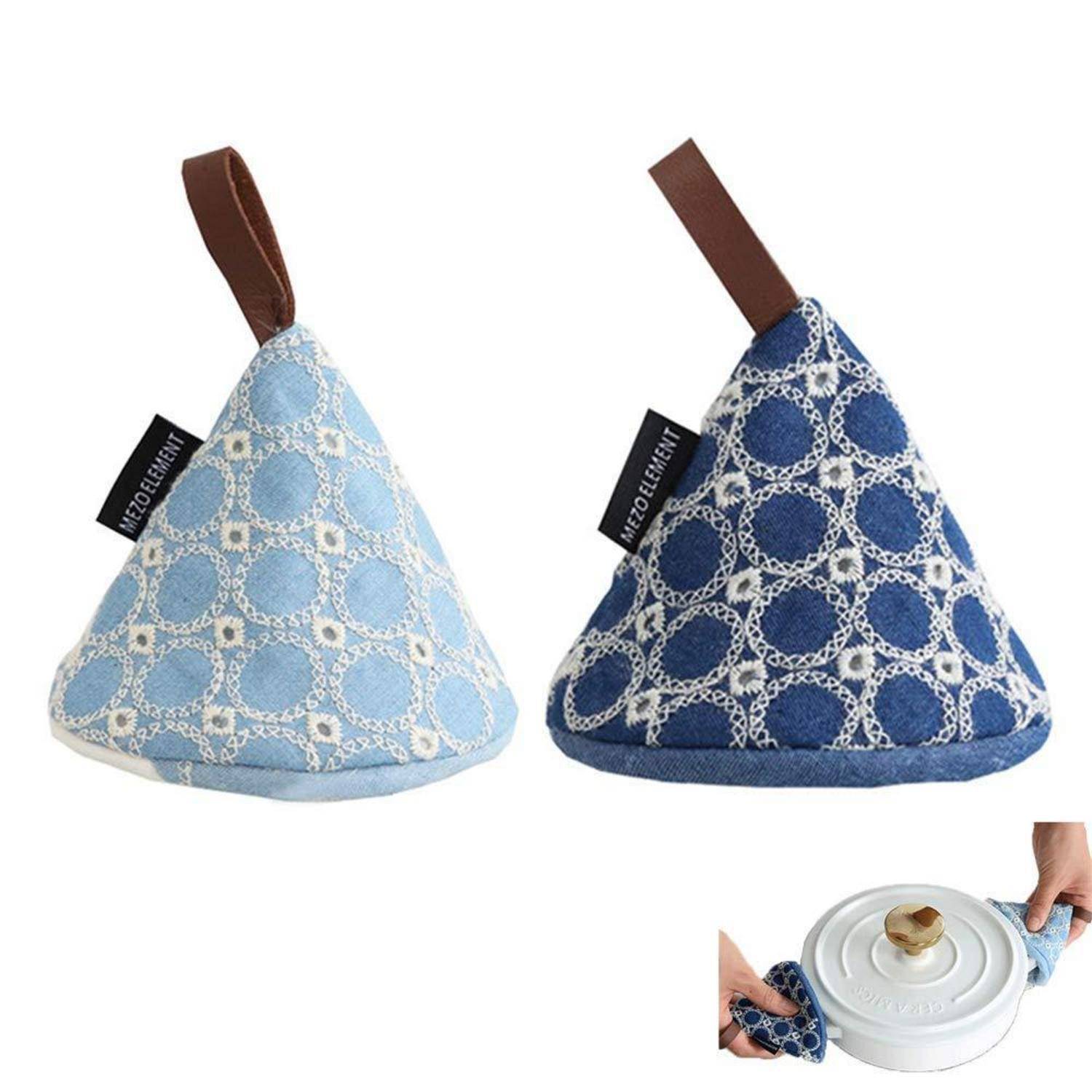 Zwei gemusterte Topflappen aus Stoff, einer hellblau und einer dunkelblau, gezeigt mit einer Hand, die einen verwendet, um einen heißen Pfannendeckelgriff zu heben.
