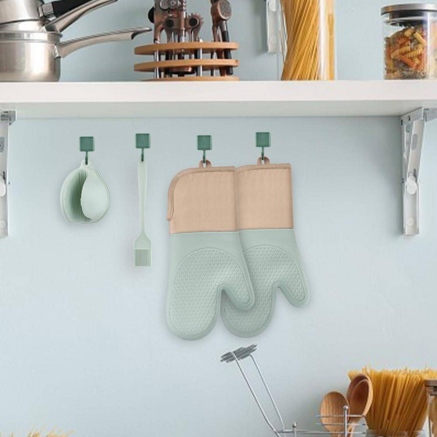 Küchenregal mit hängenden mintgrünen Utensilien und passenden Ofenhandschuhen, die an Haken vor einer hellblauen Wand befestigt sind.