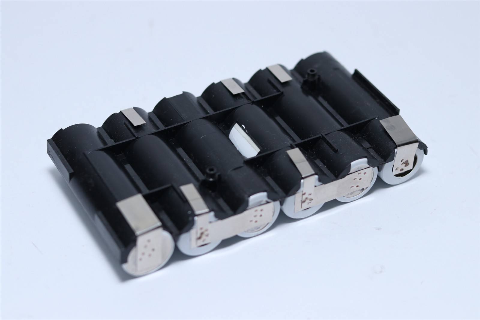 Schwarzes zylindrisches Batteriepack mit mehreren verbundenen Zellen und silbernen Kontaktenden, auf hellem Hintergrund dargestellt.