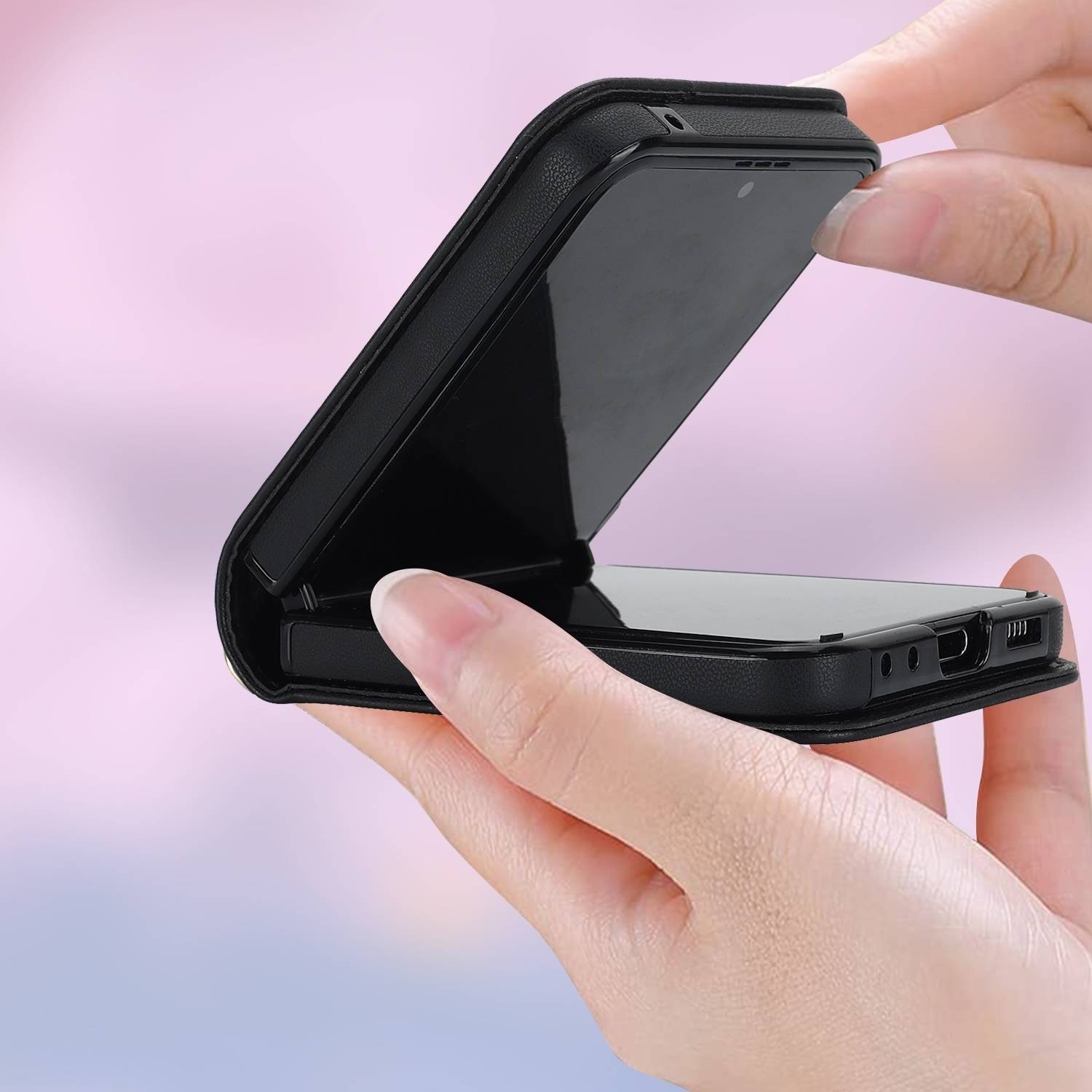 Hände öffnen ein schwarzes klappbares Handycase oder Clamshell-Gerät und zeigen einen glänzenden inneren Bildschirm vor einem pastellfarbenen Hintergrund.
