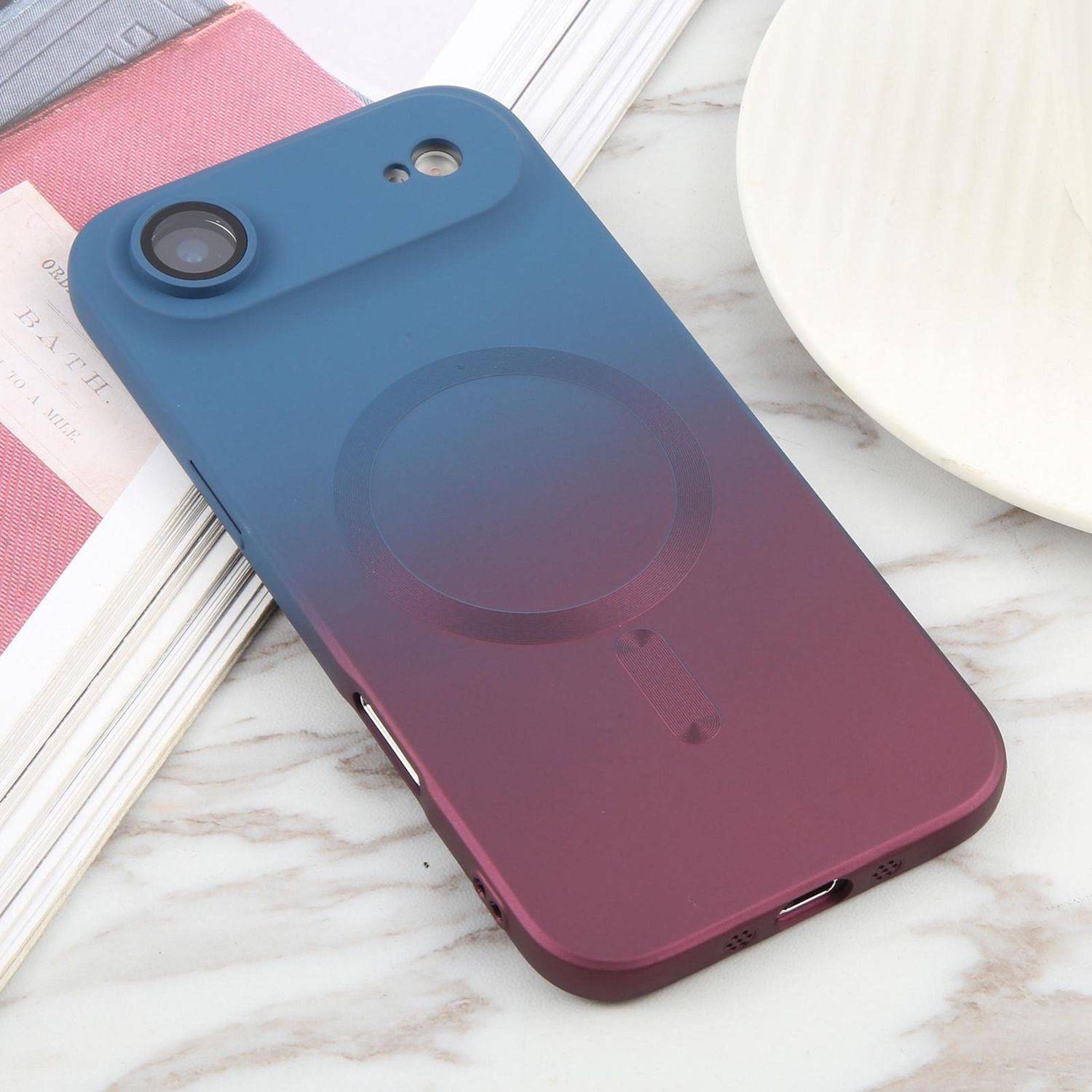 Smartphonehülle mit Farbverlauf von Blau zu Lila und kreisförmiger Magnethalterung, gezeigt auf einer Marmoroberfläche neben einem Buch und einem Teller.