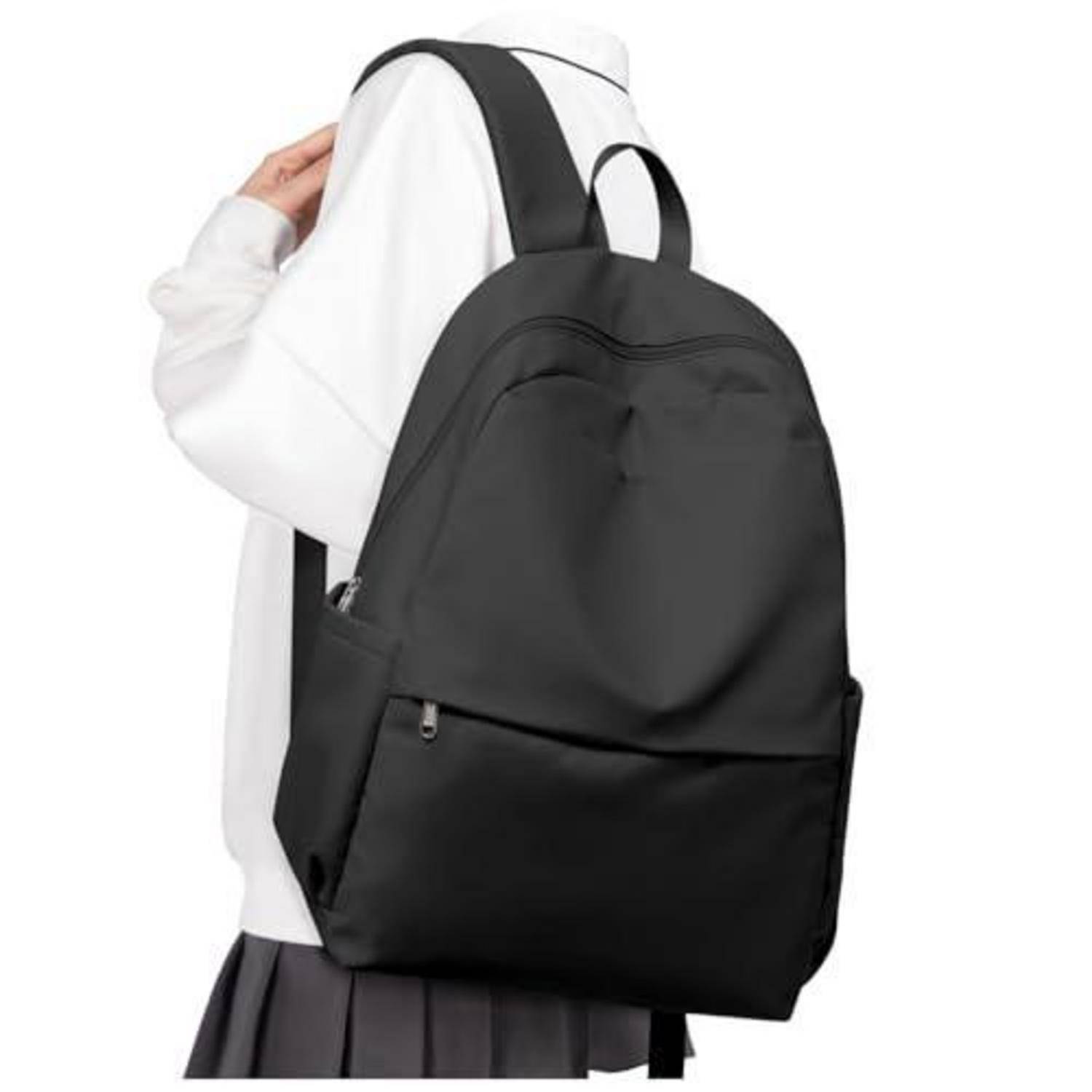 Eine Person, die einen großen schwarzen Rucksack über einem weißen Oberteil und einem grauen Rock trägt, von der Seite vor einem einfachen Hintergrund gezeigt.