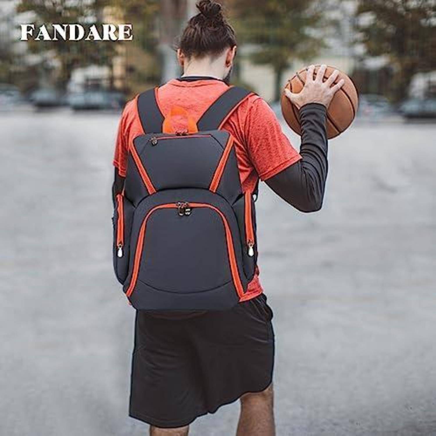 Person von hinten, die einen schwarz-roten Rucksack trägt und einen Basketball auf einem gepflasterten Platz im Freien hält.