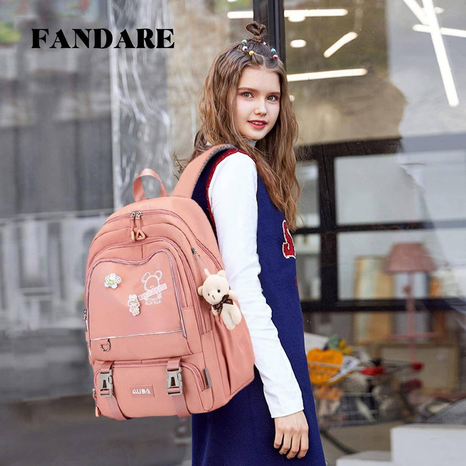 Junges Mädchen, das einen rosa Rucksack mit einem Teddybär-Anhänger trägt, steht draußen vor einem Geschäft; 'FANDARE' erscheint in der Ecke.